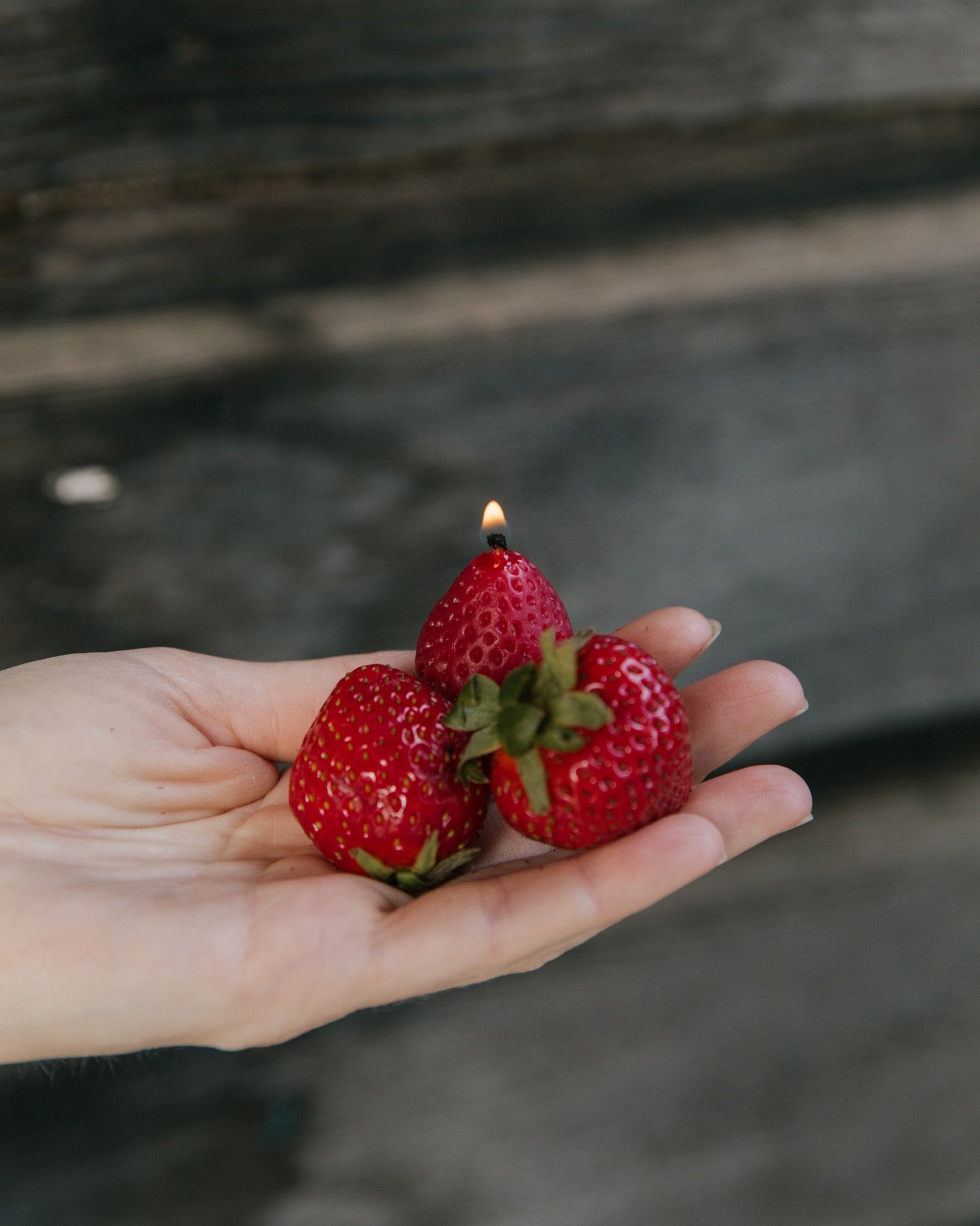 Three strawberries with candles inside held in a hand against a dark background