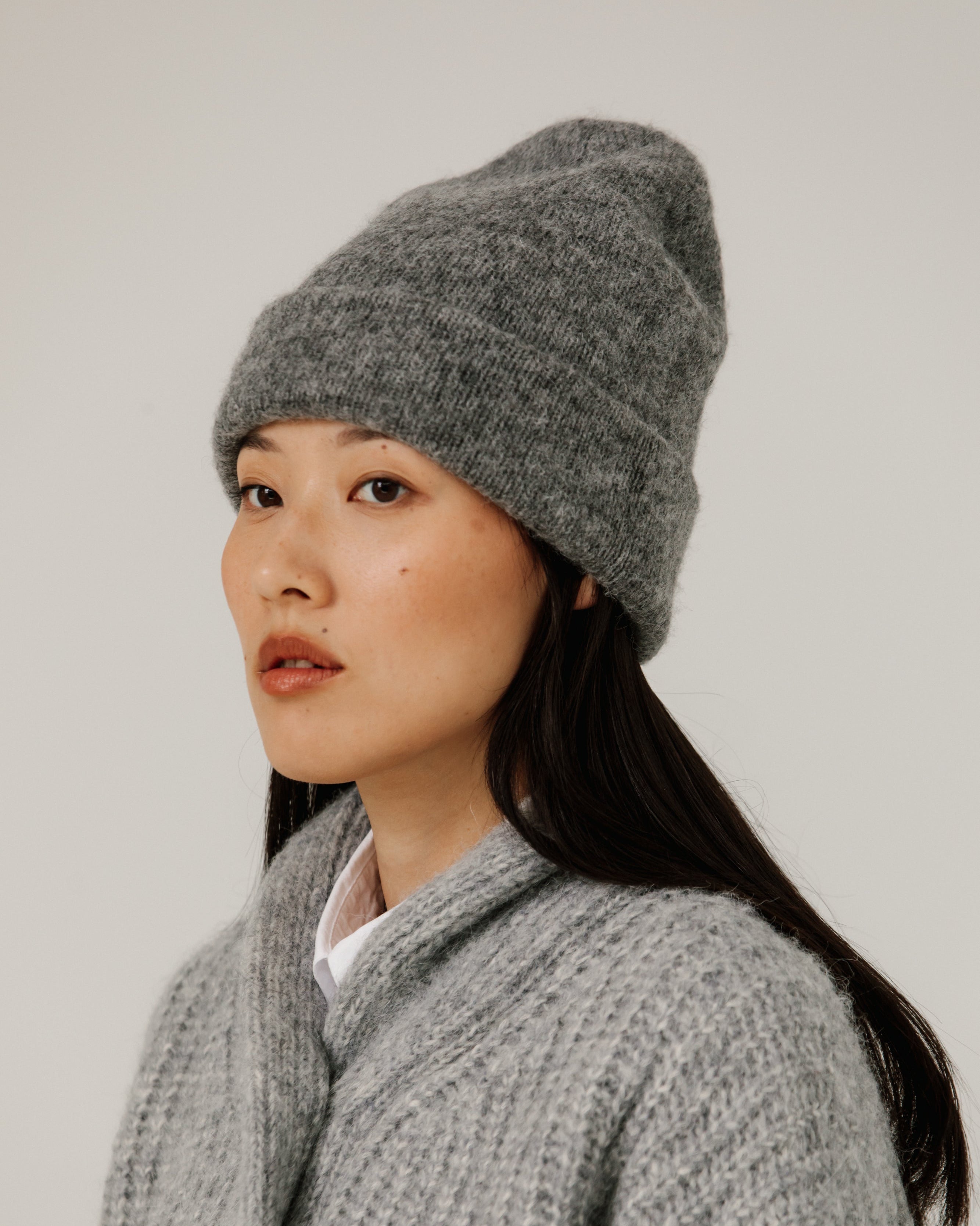 Woman wearing a gray knit beanie and sweater against a plain background