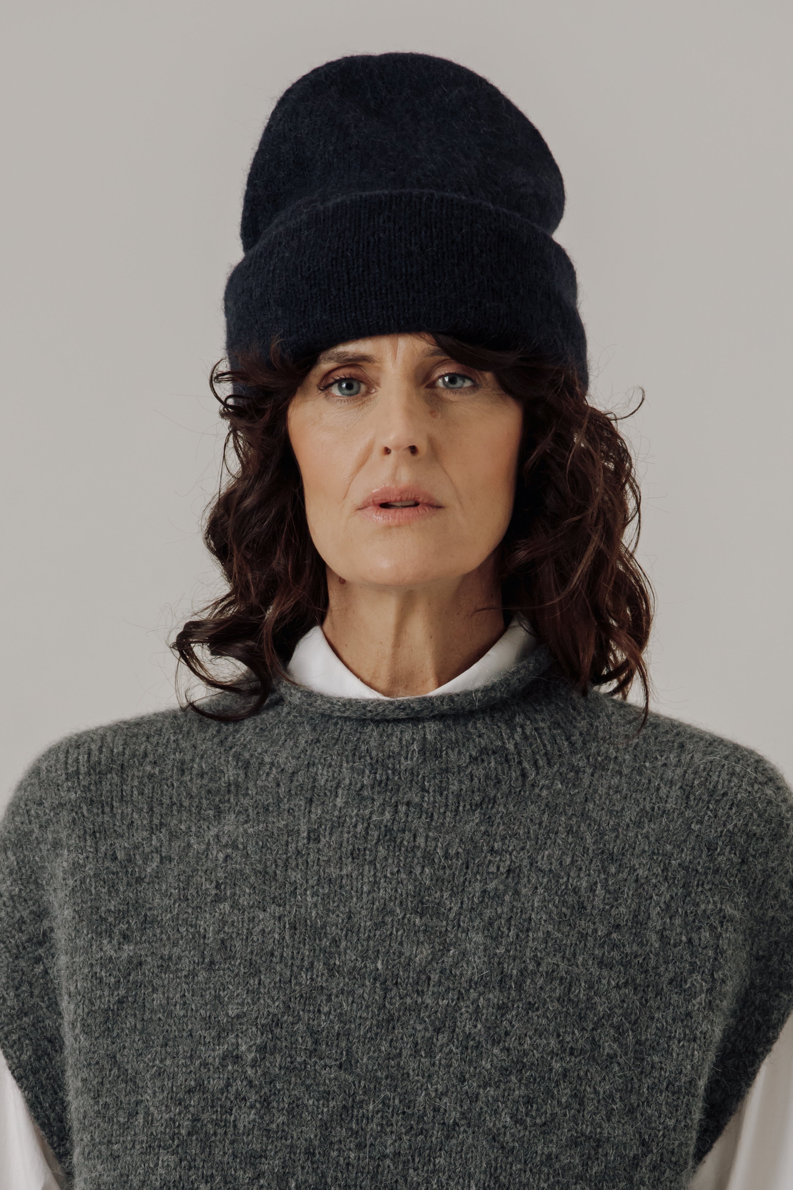 Woman wearing a dark knit beanie and gray sweater against a plain background