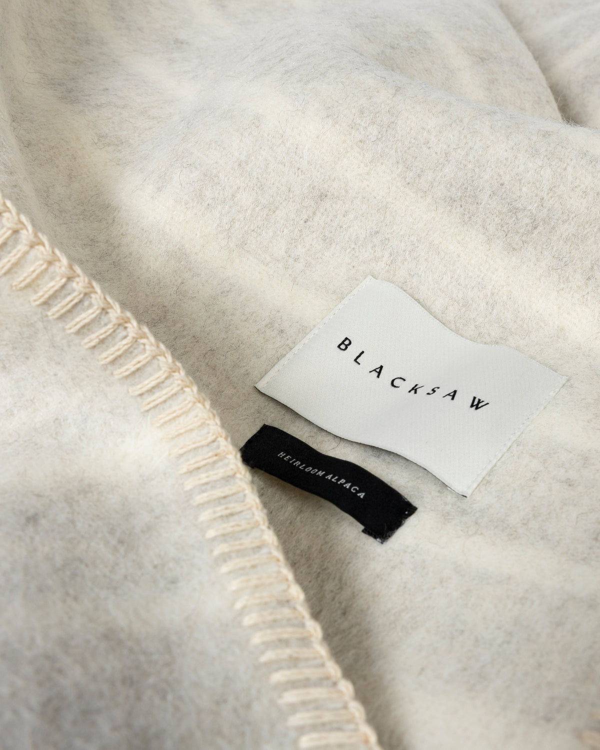 Close-up of a soft cream-colored knit fabric with a visible white sewn-in label reading BLACKSAW and a small black brand tag.