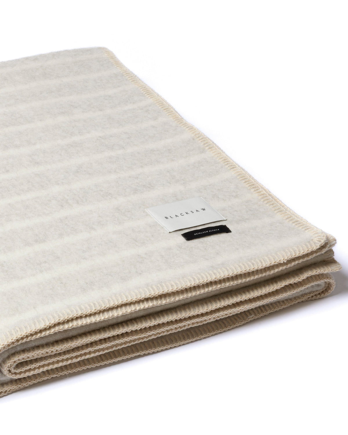 A folded cream and beige striped knit blanket with a small white brand tag, shown on a clean white background.
