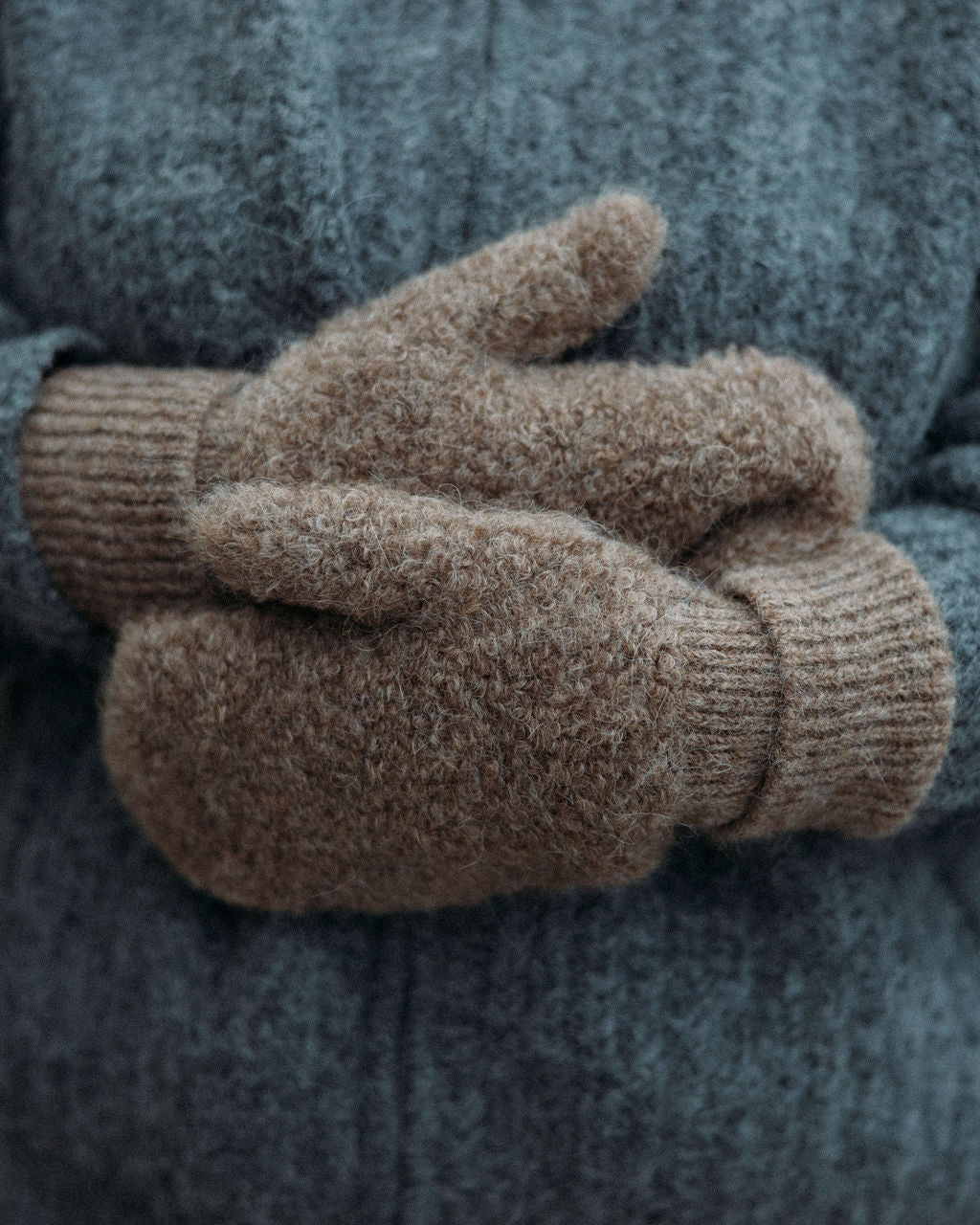 Pair of brown Bare Knitwear mittens held against a gray sweater