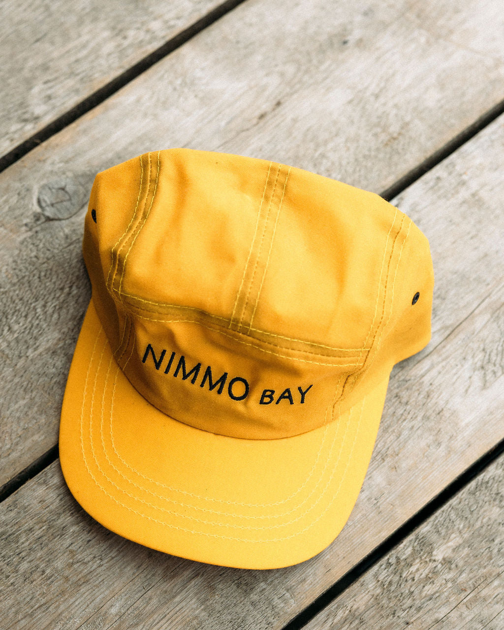 Yellow anian tin cap with 'Nimmo Bay' text on a wooden surface