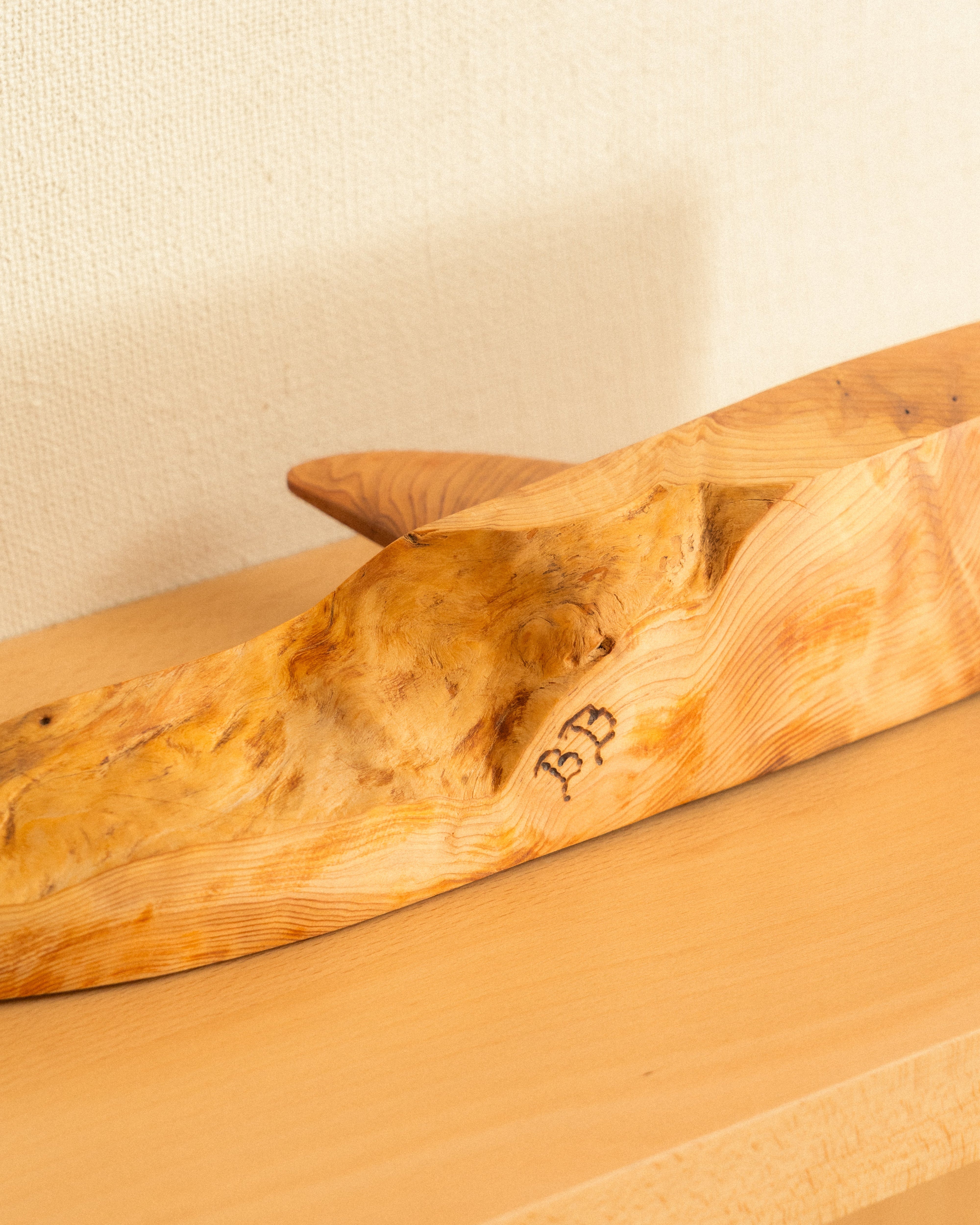 Wooden orca carving, bottom, with artist initials on a beige surface