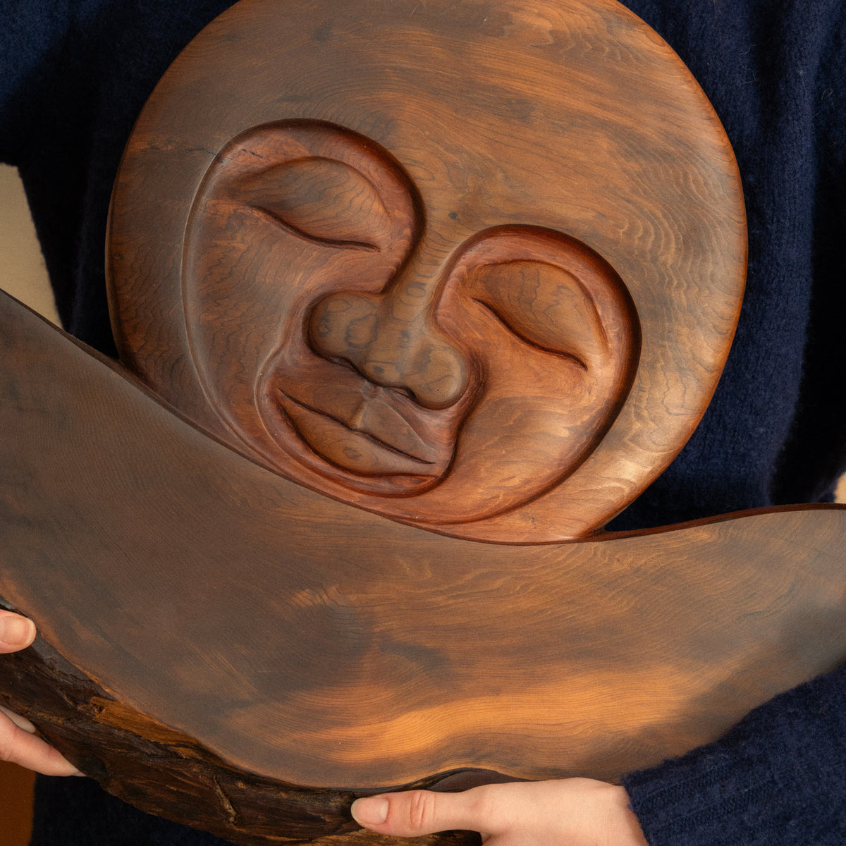 Person holding a large wooden carving with a face design.