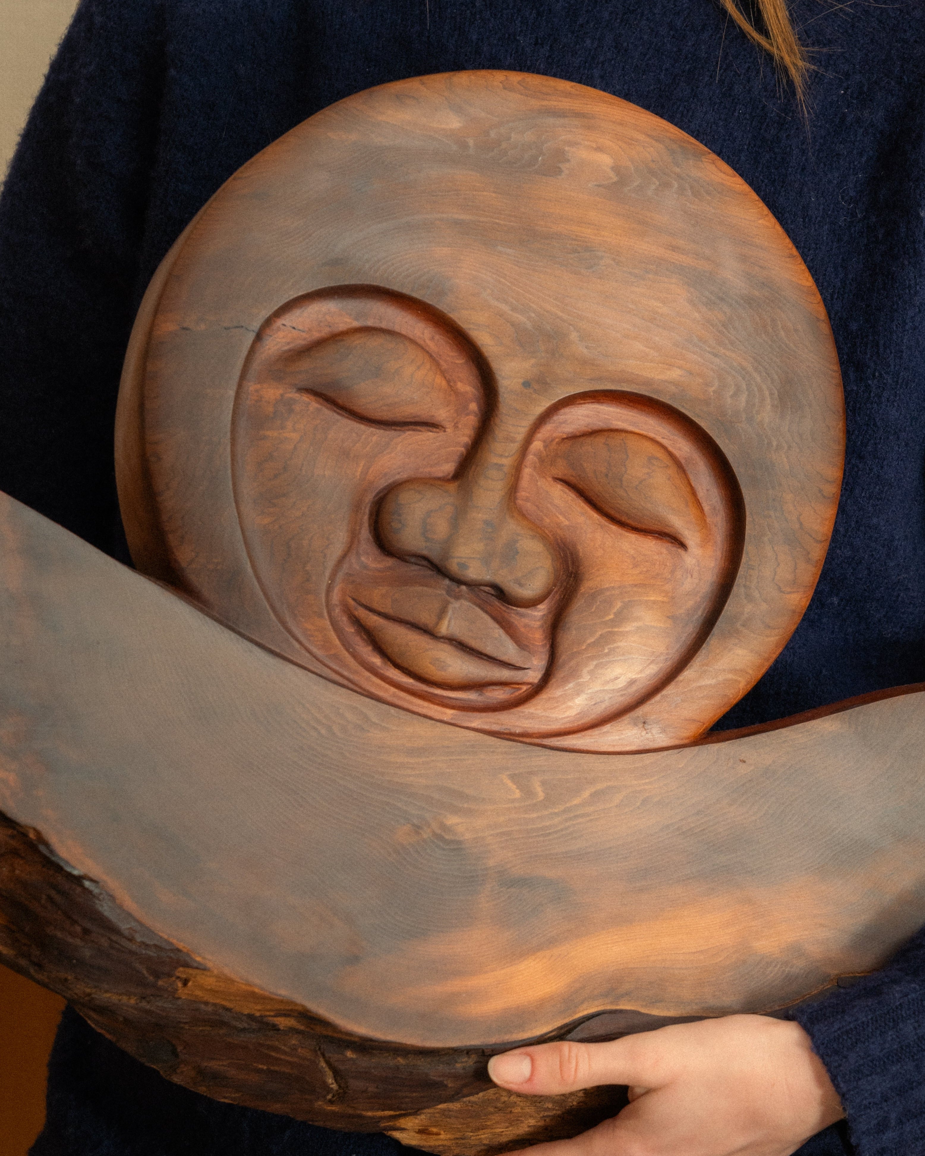 Person holding a large wooden carving with a Moon face design.