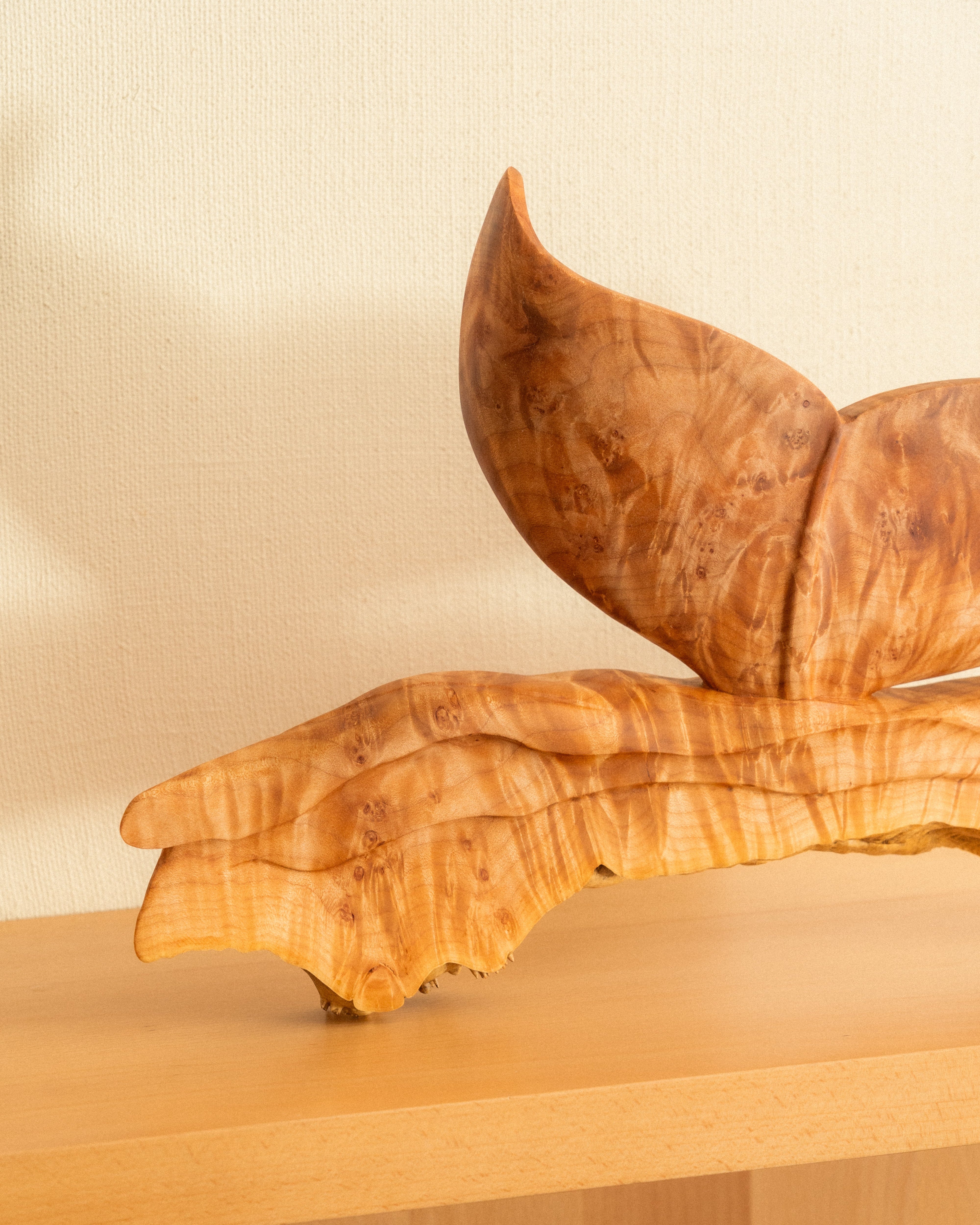 Wooden sculpture of a whale tale on a wooden shelf with a plain background