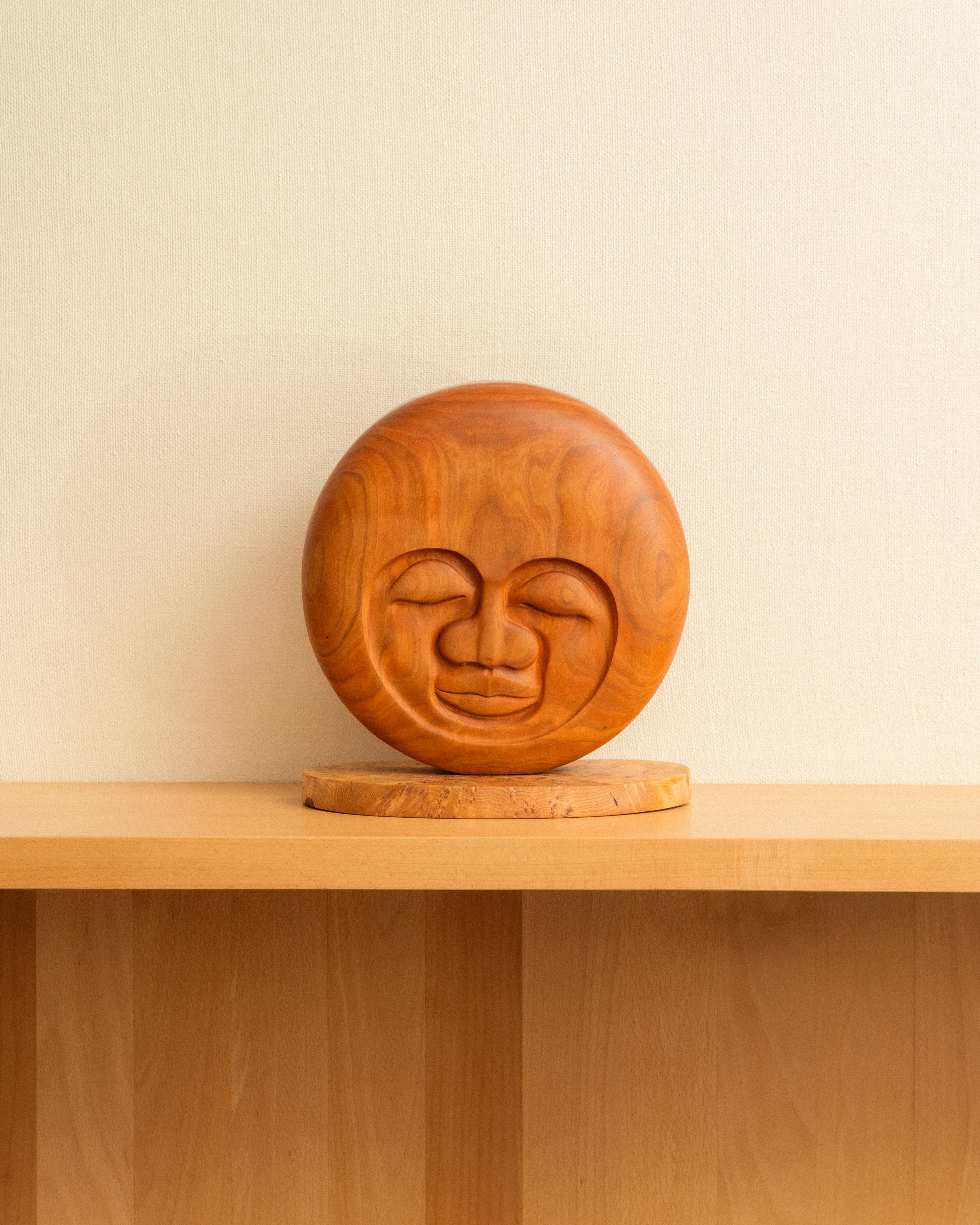 Wooden sculpture of a Moon on a wooden shelf with a beige wall background
