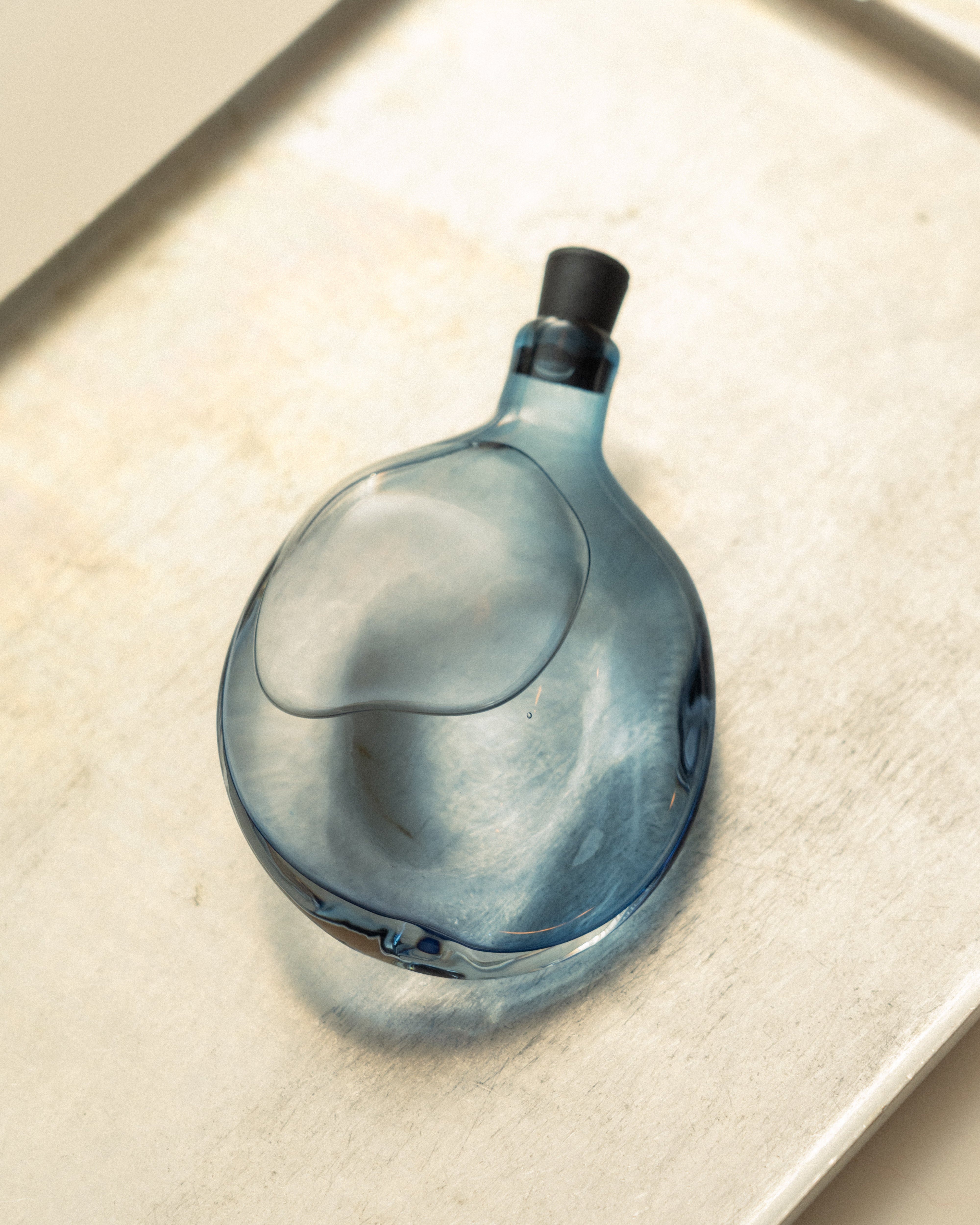 Blue glass flask with a black cap on a beige surface