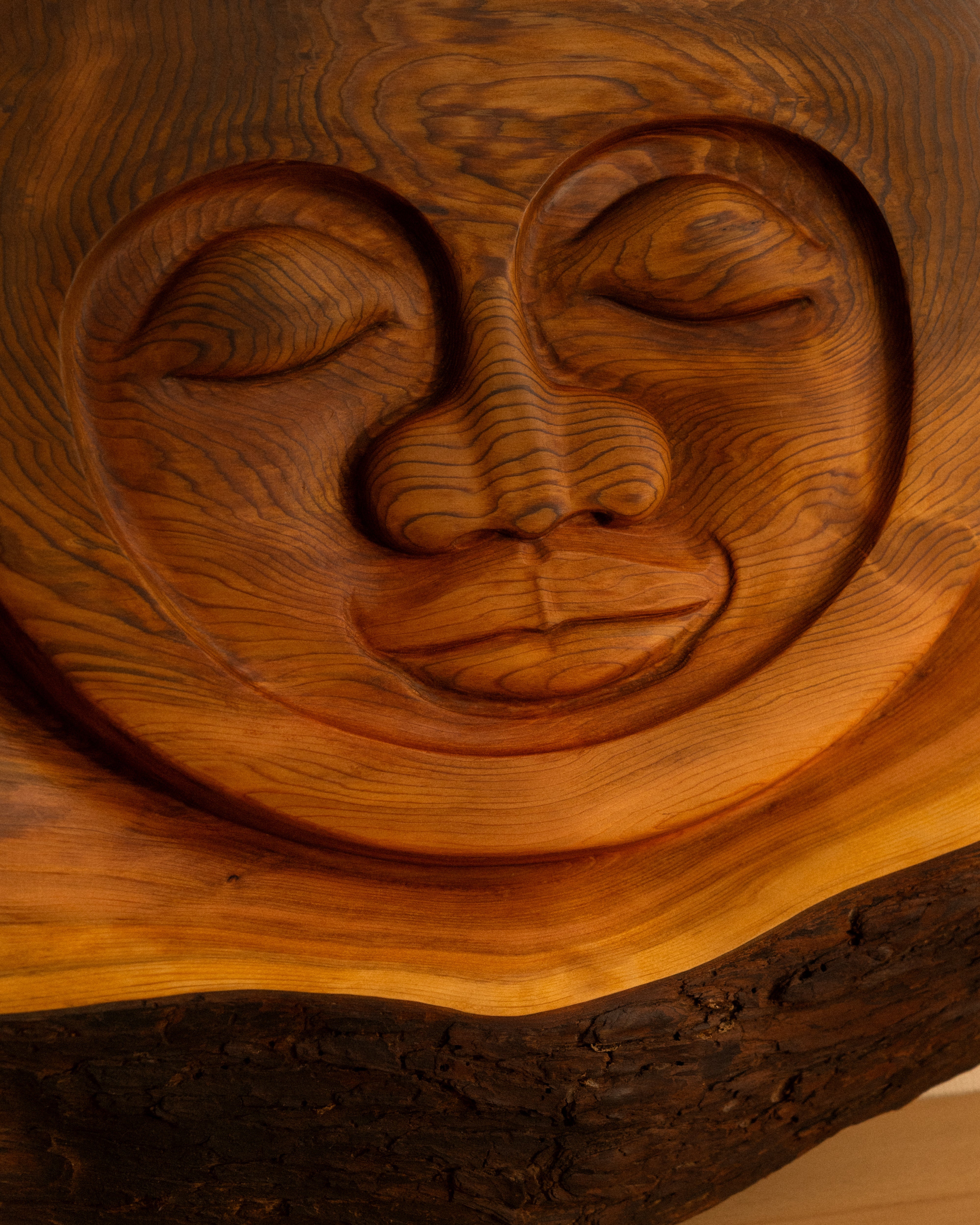 Wooden carving of a sun face with a serene expression on a wooden background