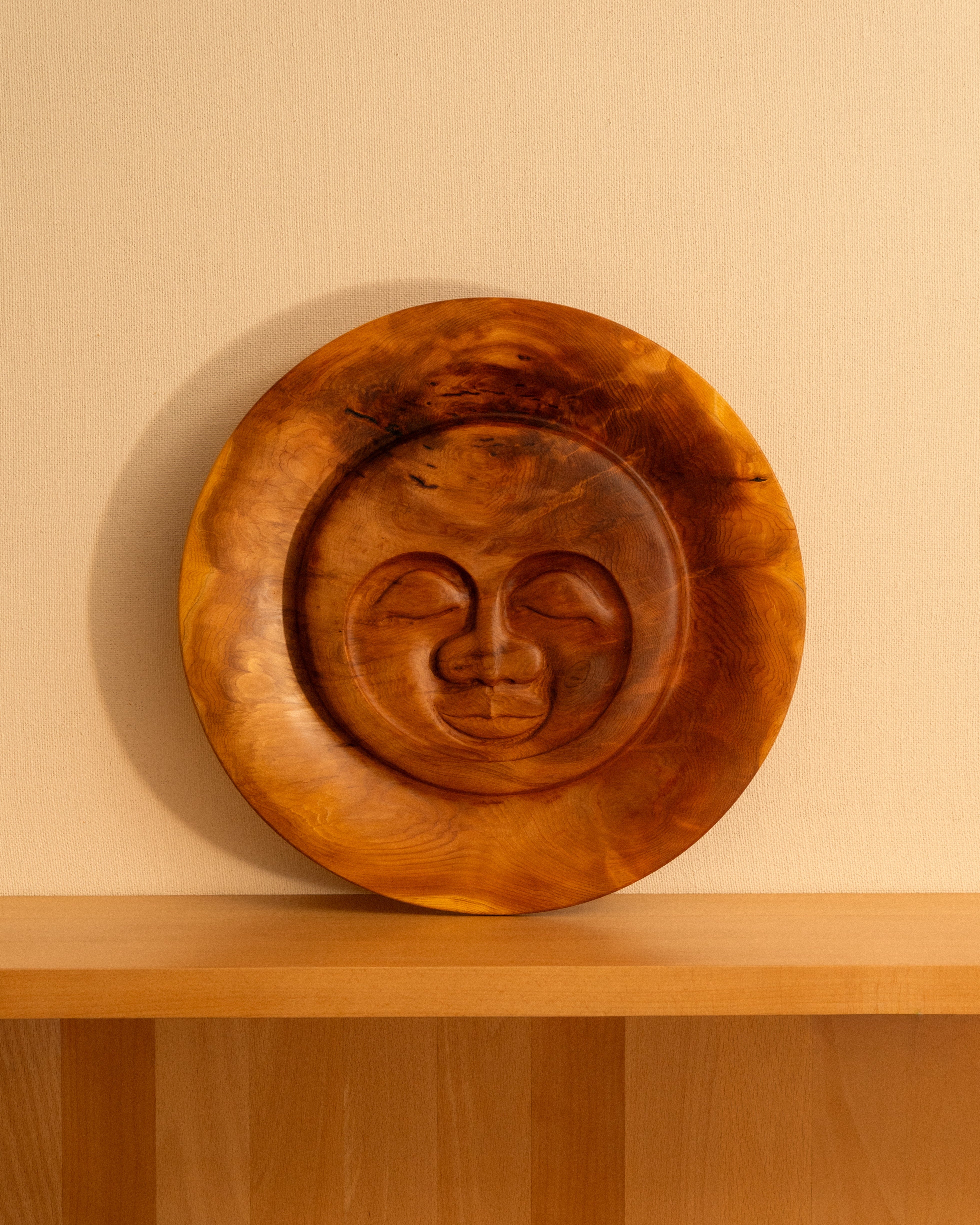 Serenity Sun carving by Bjorn Banke against a tan wall.