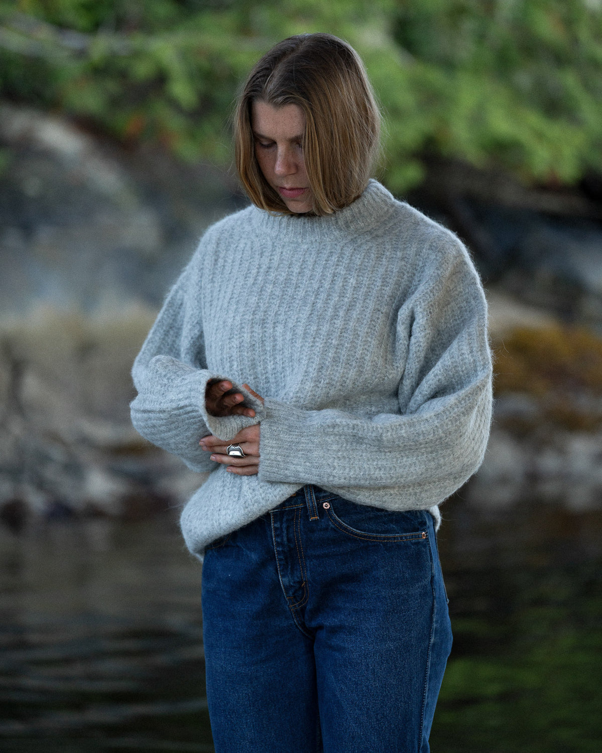 Woman wearing a bare knitwear lofty alpaca crewneck with a coastal background.