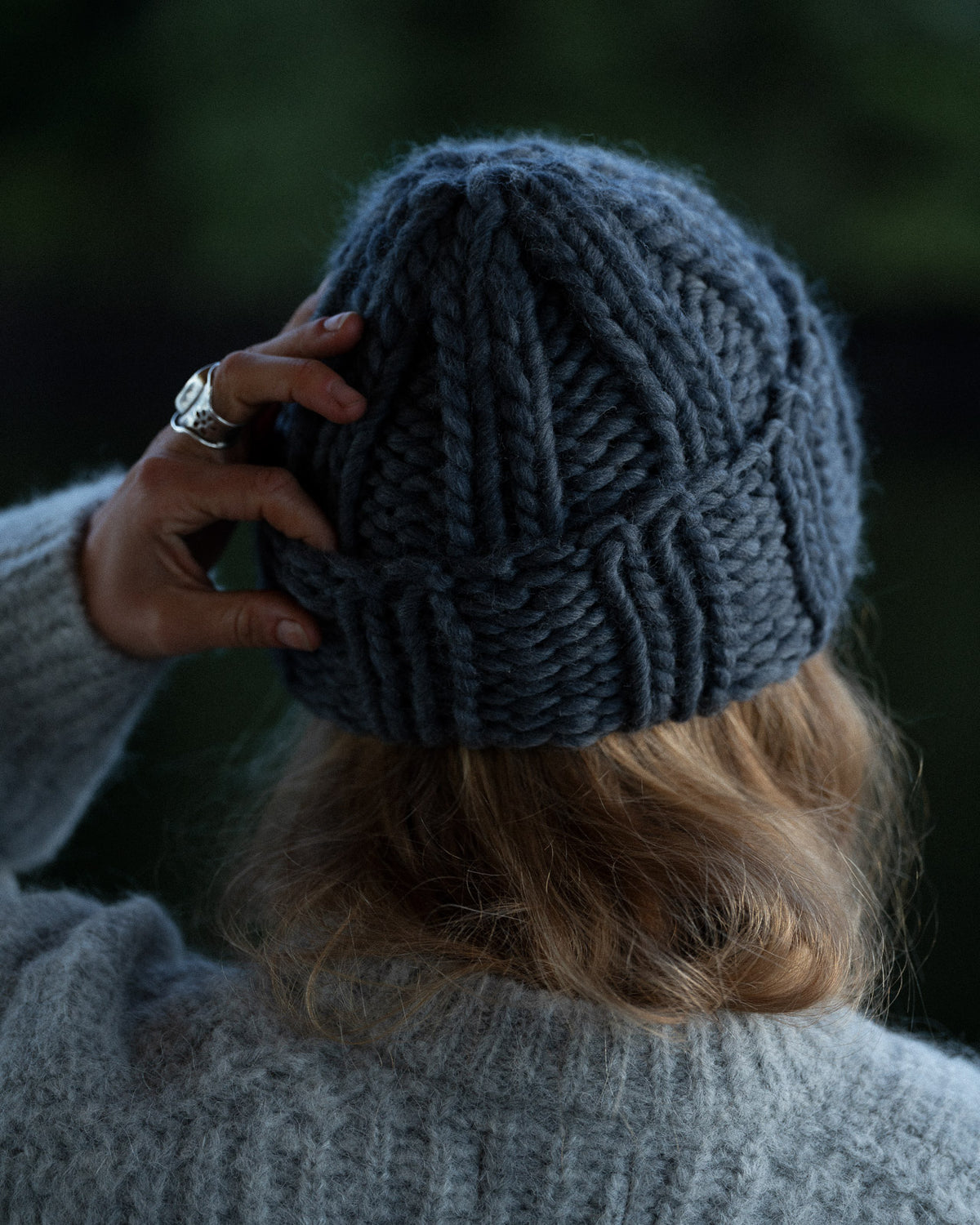 a woman from behind wearing a toque and knit sweater against a background of trees