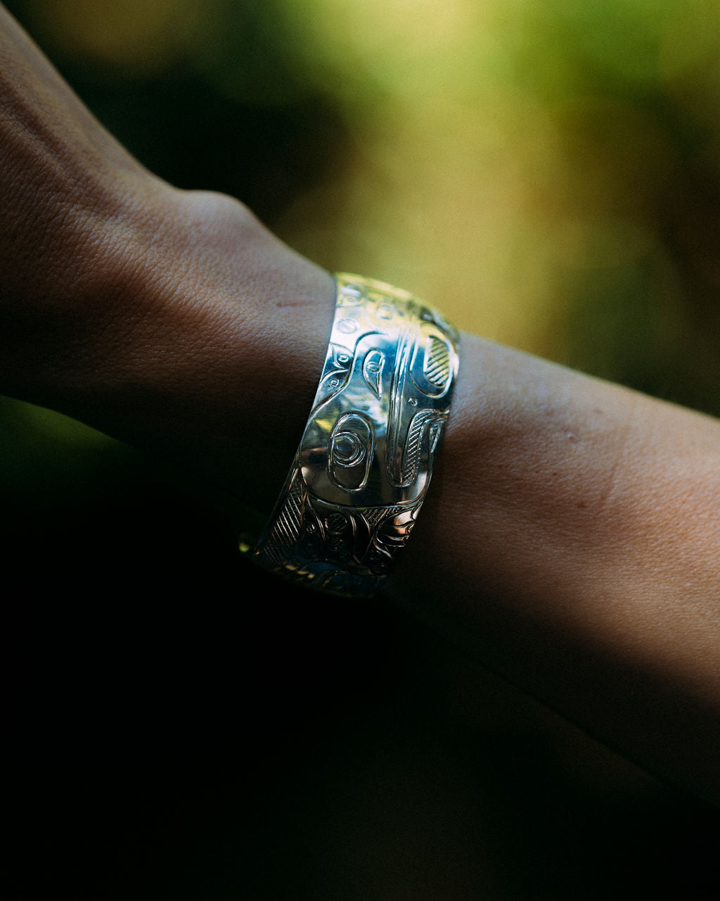 Deb Hunt indigenous carved frog bracelet on a wrist with forest background