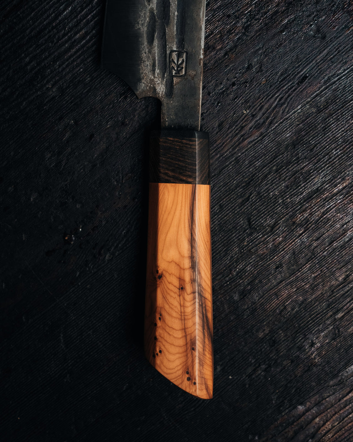 A close up of the handle of a leechtown blacksmith forged steel knife on a black wooden background