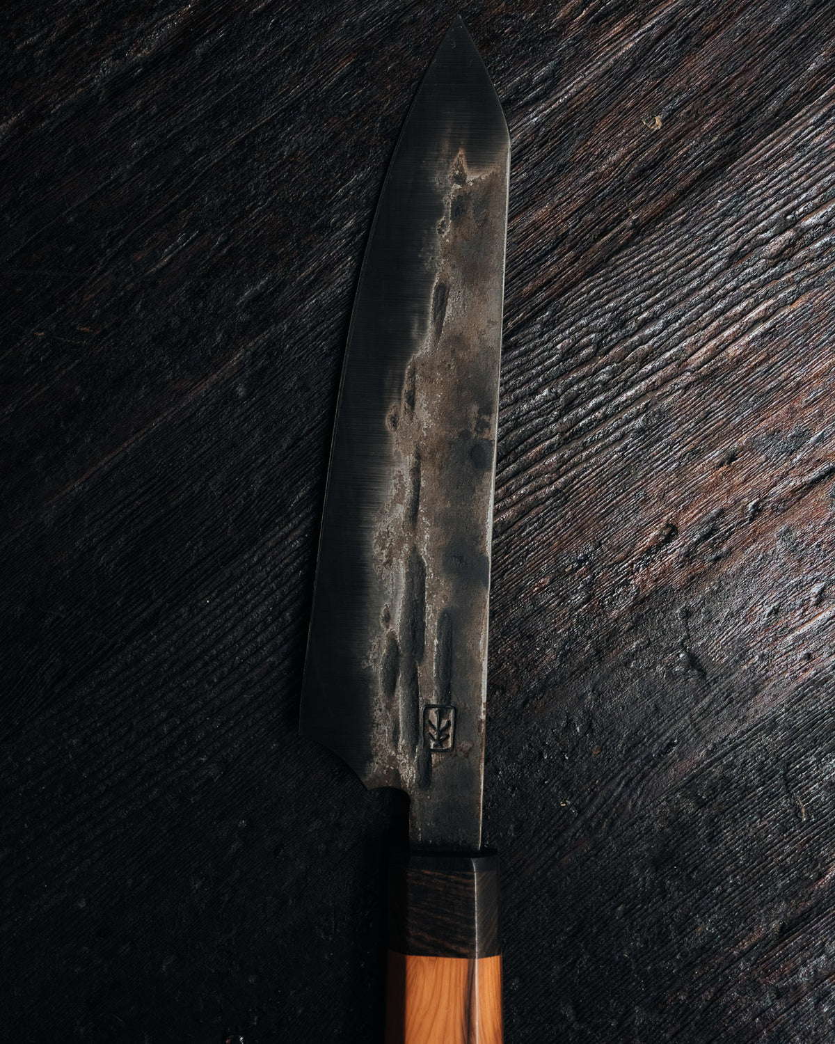 A close up of the blade of a leechtown blacksmith forged steel knife on a black wooden background
