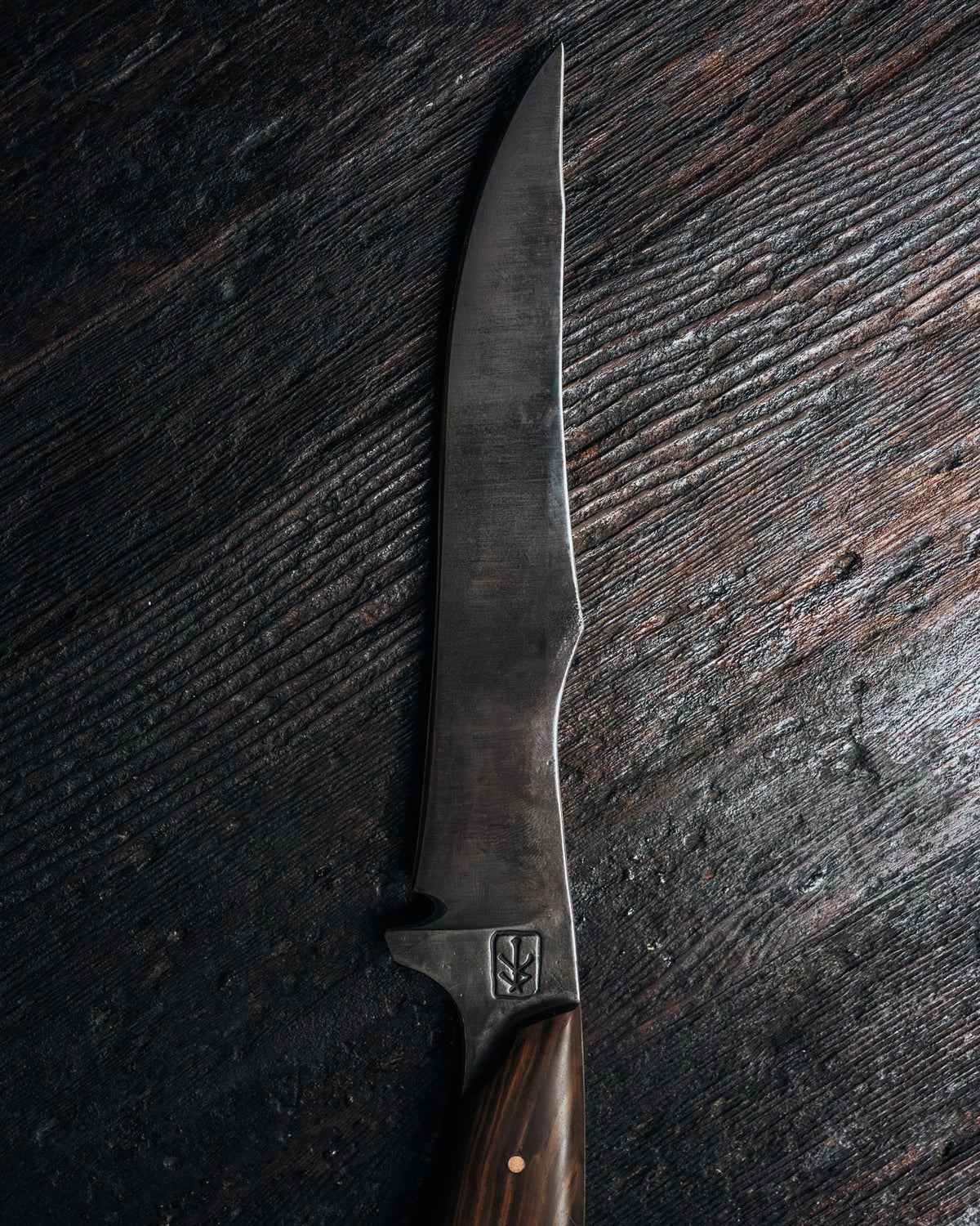 a forged steel blade of a knife on a black wooden background.