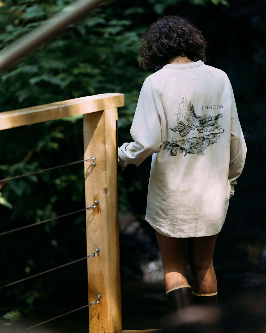 Woman wearing a pelican anian henley with a nimmo bay topical map pn the back, walking down stairs