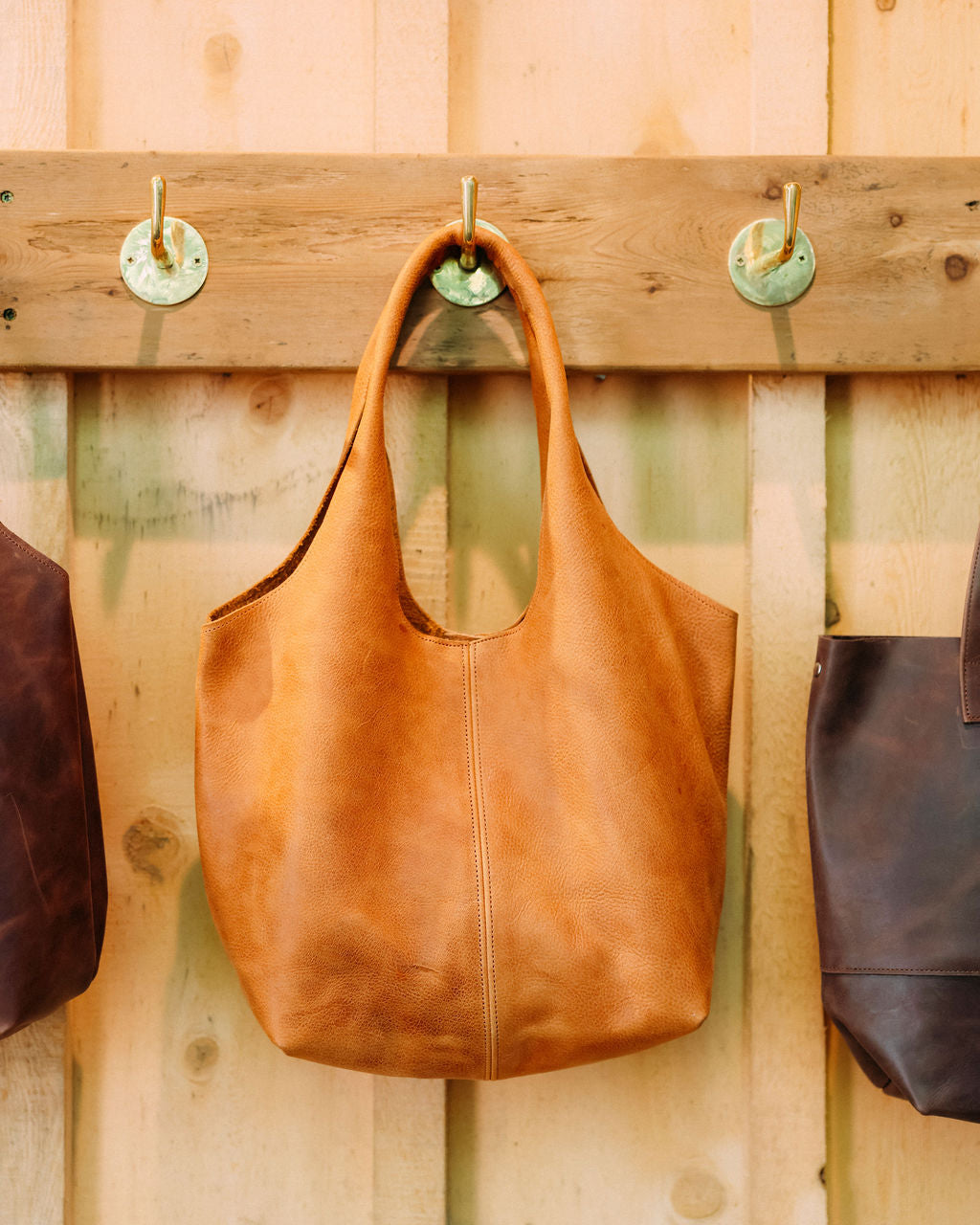 Brown leather handbag hanging on a wooden wall with hooks