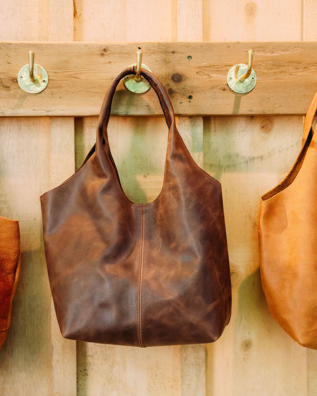 Brown leather handbag hanging on a wooden wall with hooks