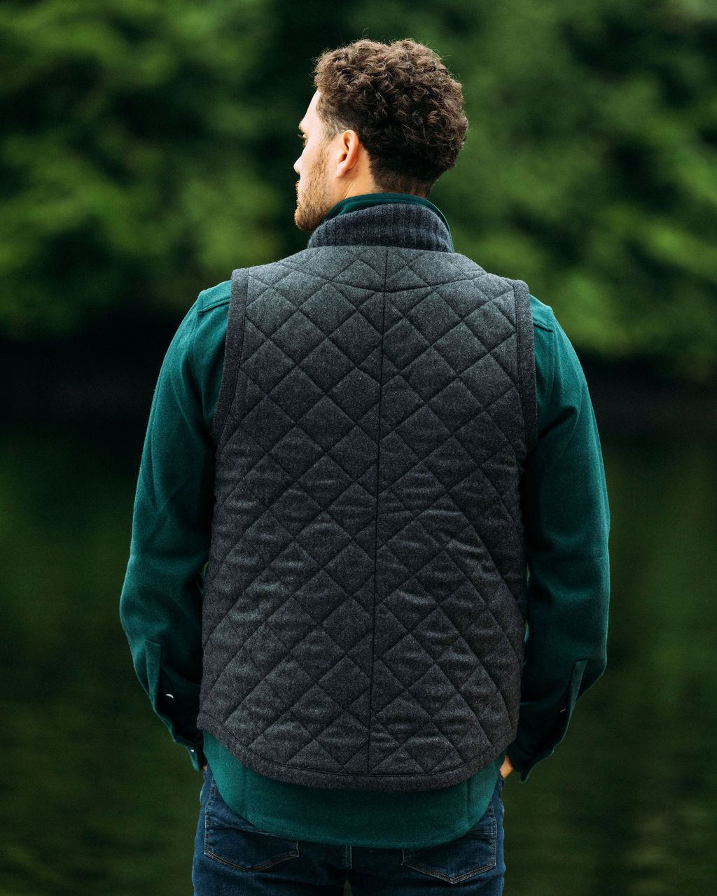 Man wearing a quilted vest over a green shirt with a blurred green background