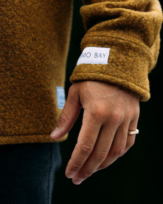 Close-up of a person wearing a mustard yellow jacket with a brand label on a black background