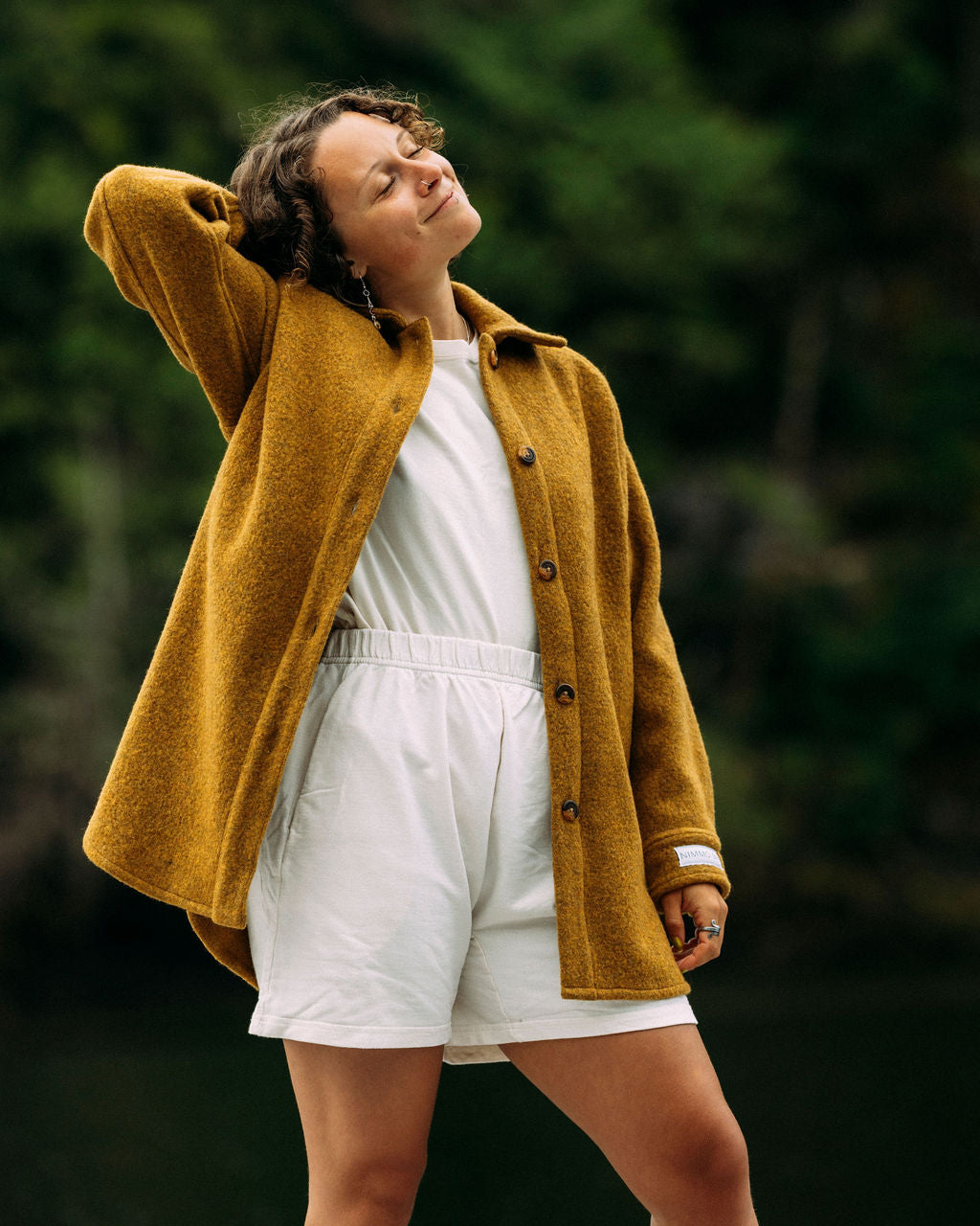 Person wearing a mustard yellow coat over a white outfit with a blurred green background