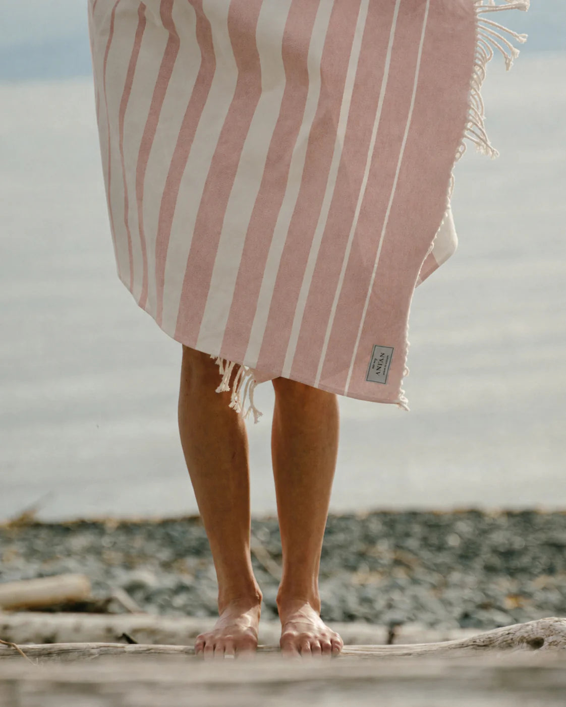 Person standing on a beach with a pink and white striped towel draped over them