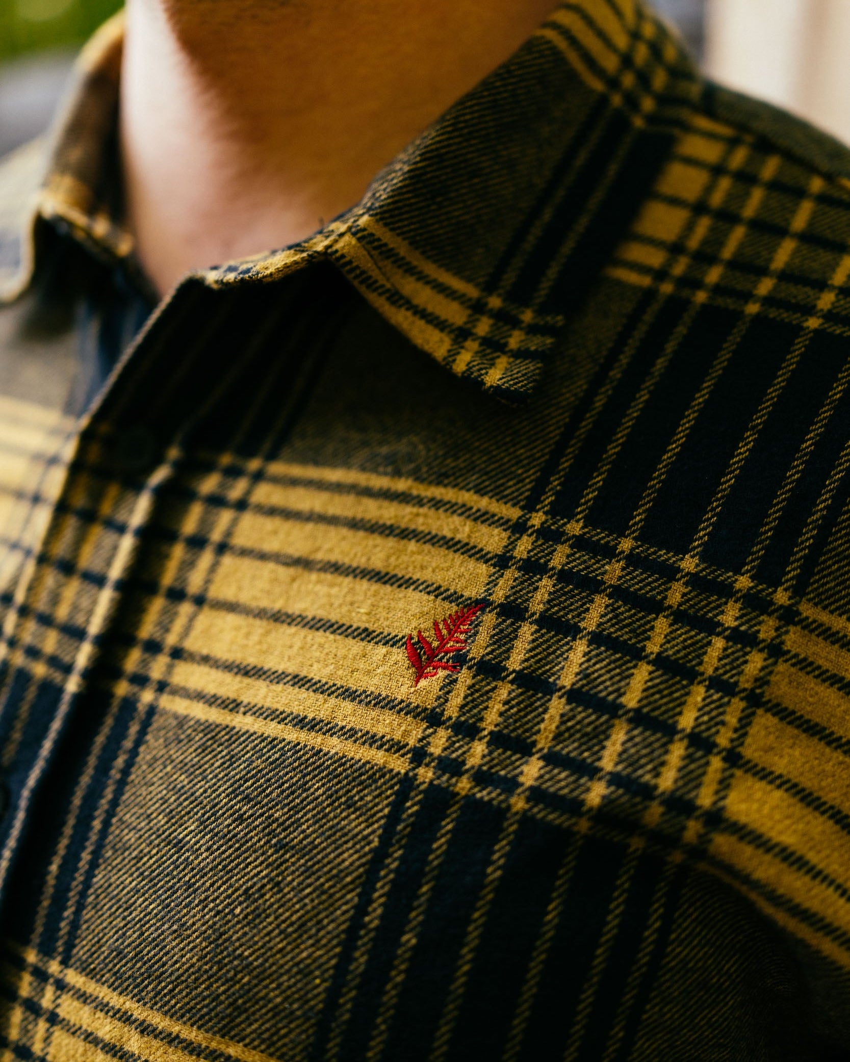 Close-up of a person wearing a plaid shirt with a small embroidered logo.