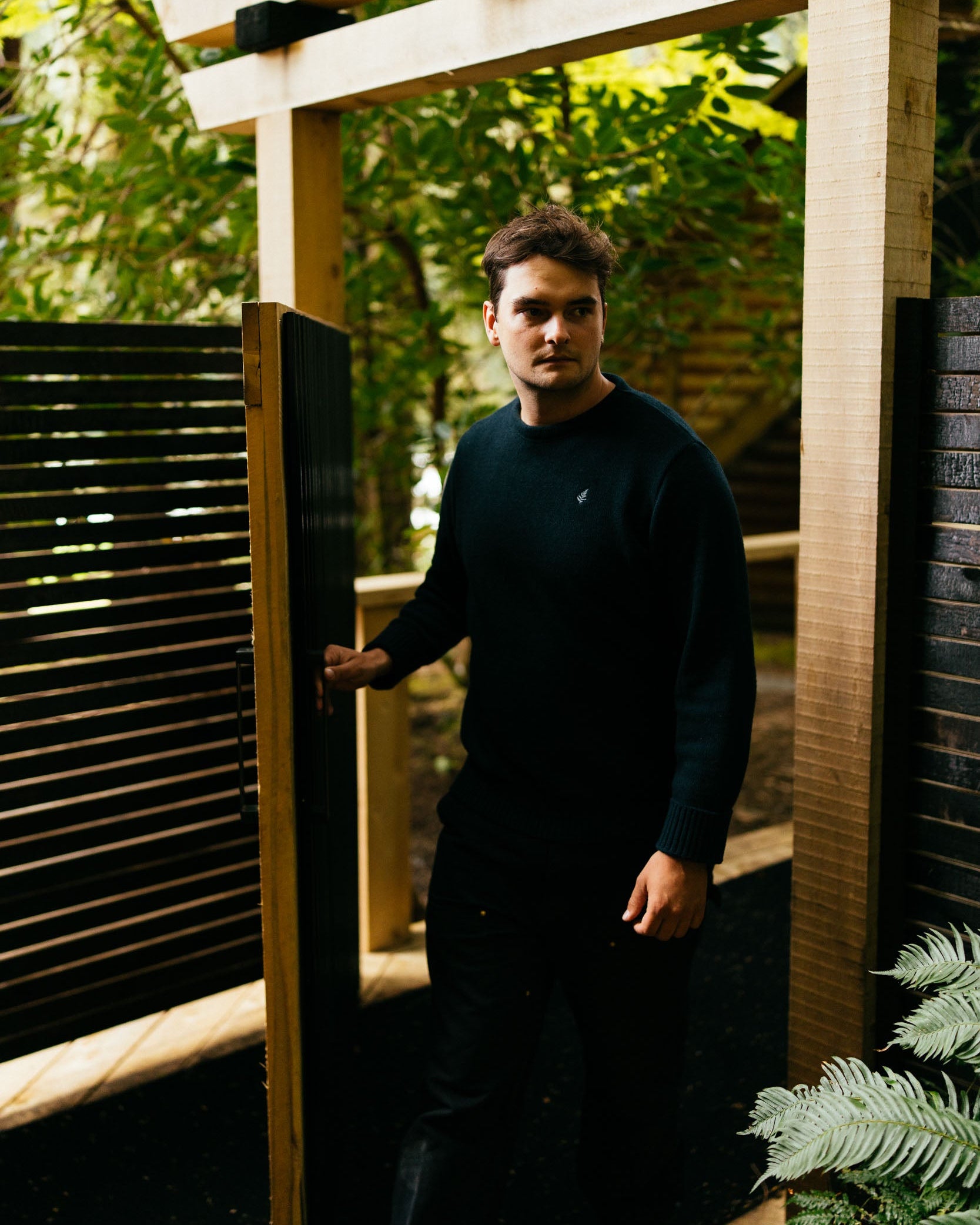 Man standing under a wooden pergola with greenery in the background