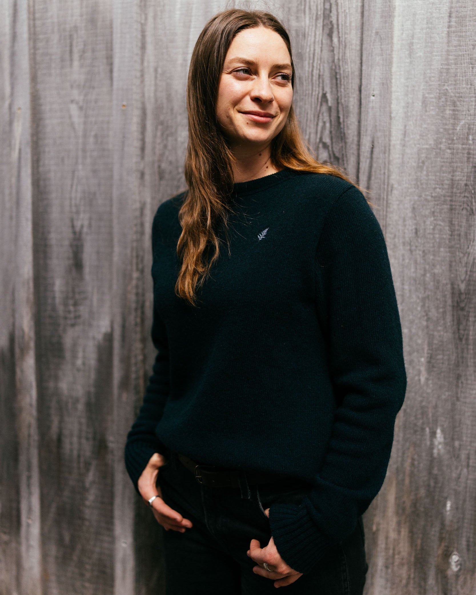 Woman wearing a dark green sweater against a wooden paneled wall