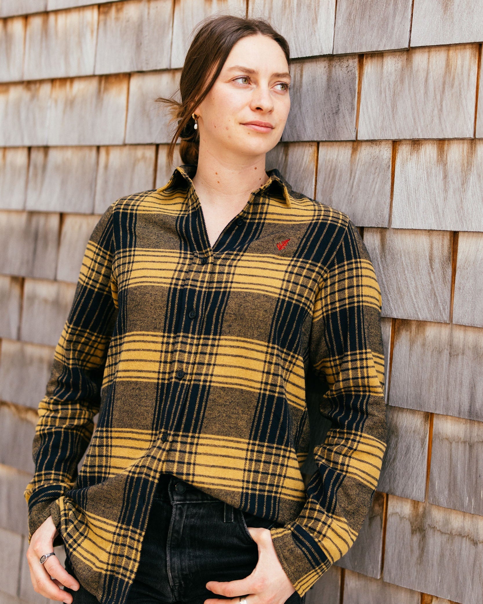 Woman wearing a yellow and black plaid shirt against a wooden wall.