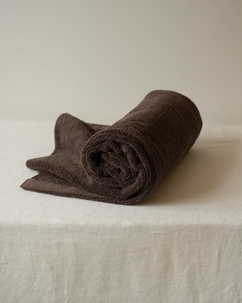 Rolled brown towel on a white surface with a neutral background