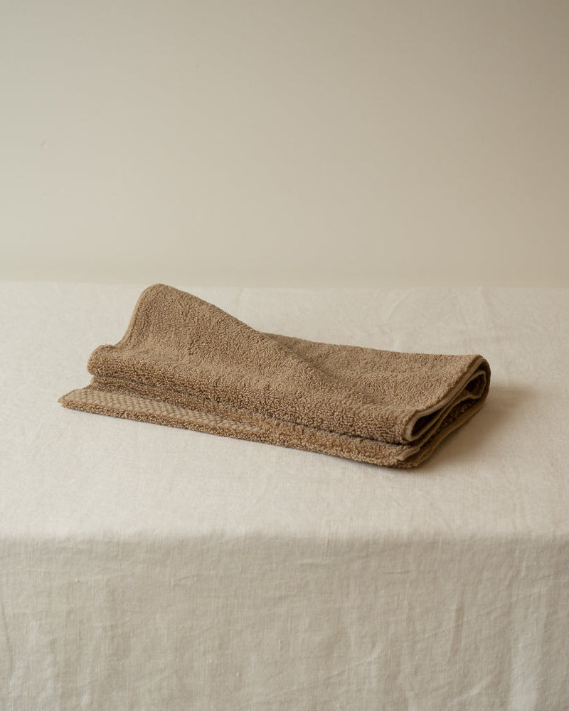 Folded beige towel on a white surface with a neutral background