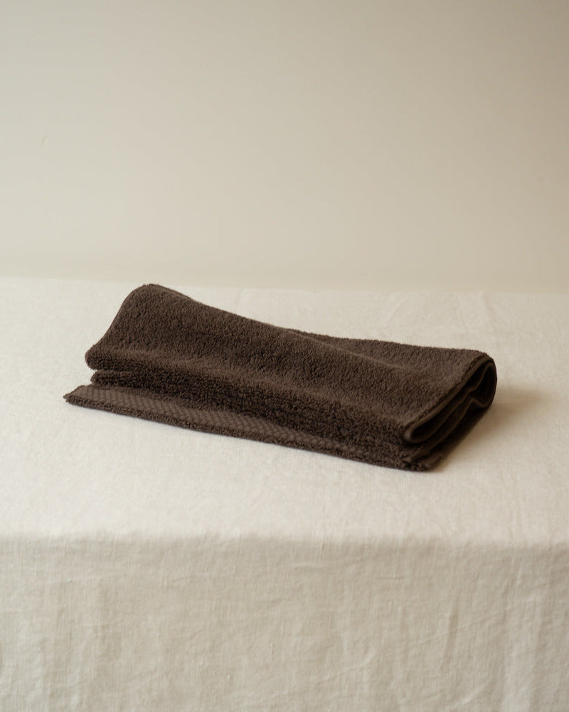 Folded brown towel on a white surface with a beige background