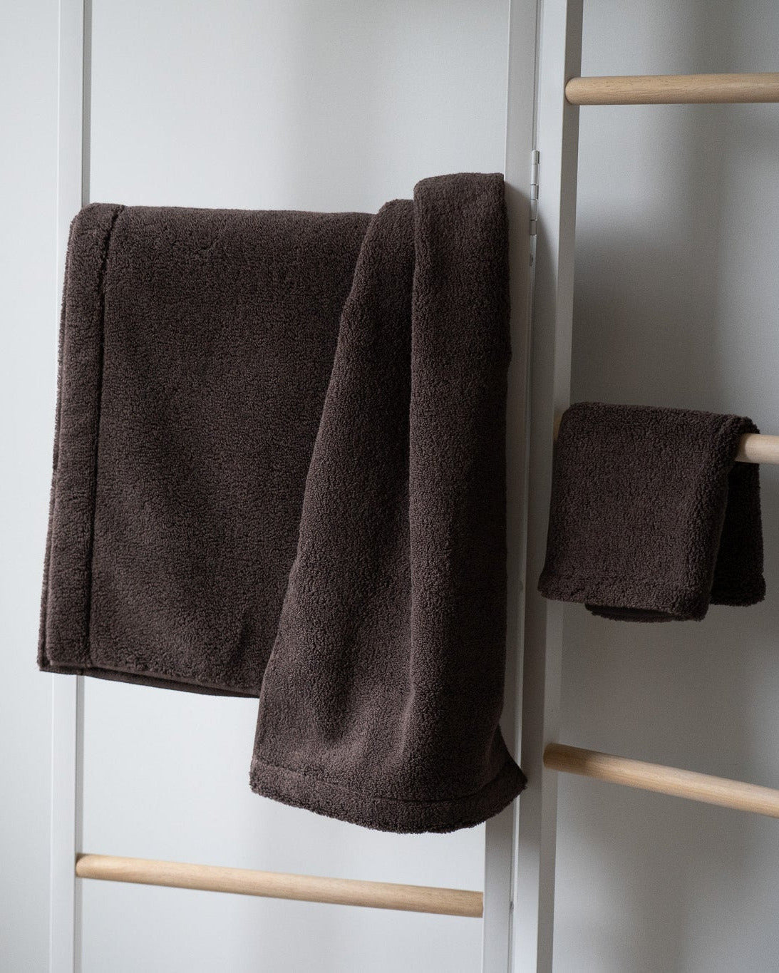 Brown towel hanging on a wooden towel rack against a white wall