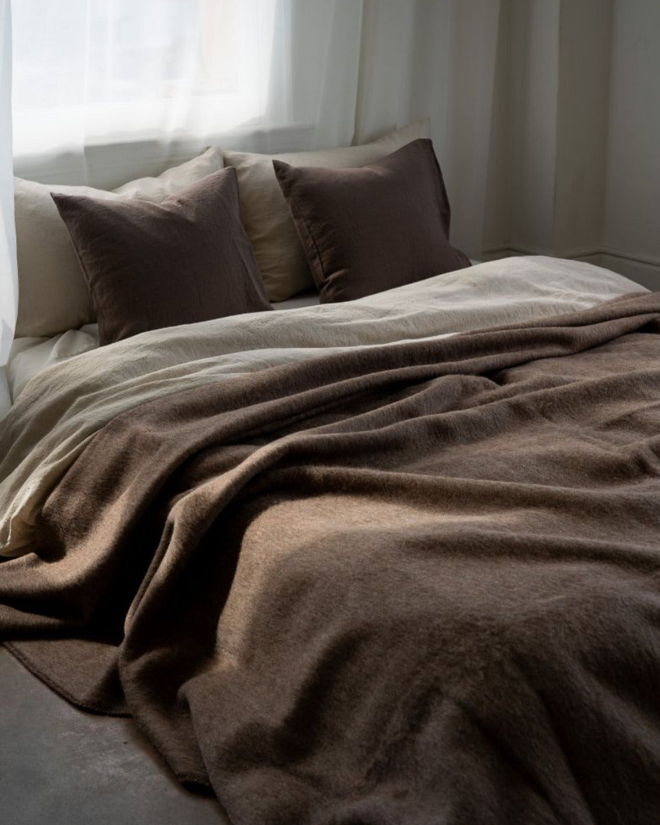 Brown blanket and pillows on a bed with a neutral color scheme