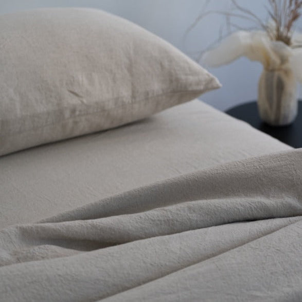 Beige textured bed sheets and pillow on a bed with a neutral background