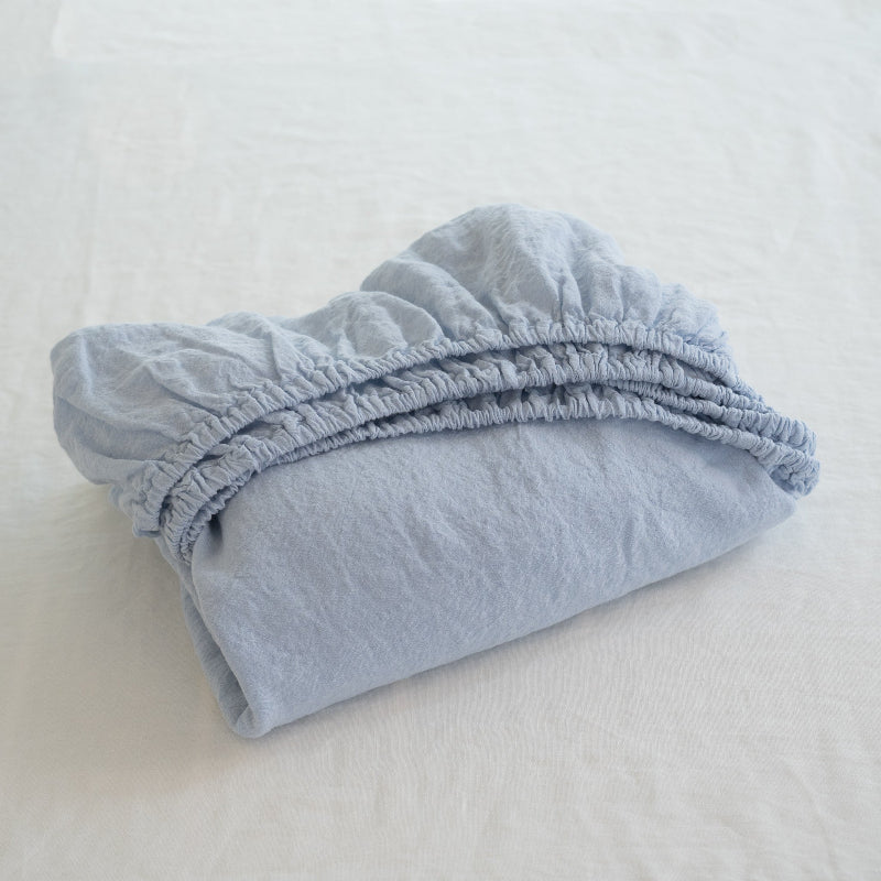Folded light blue fitted sheet on a white bed