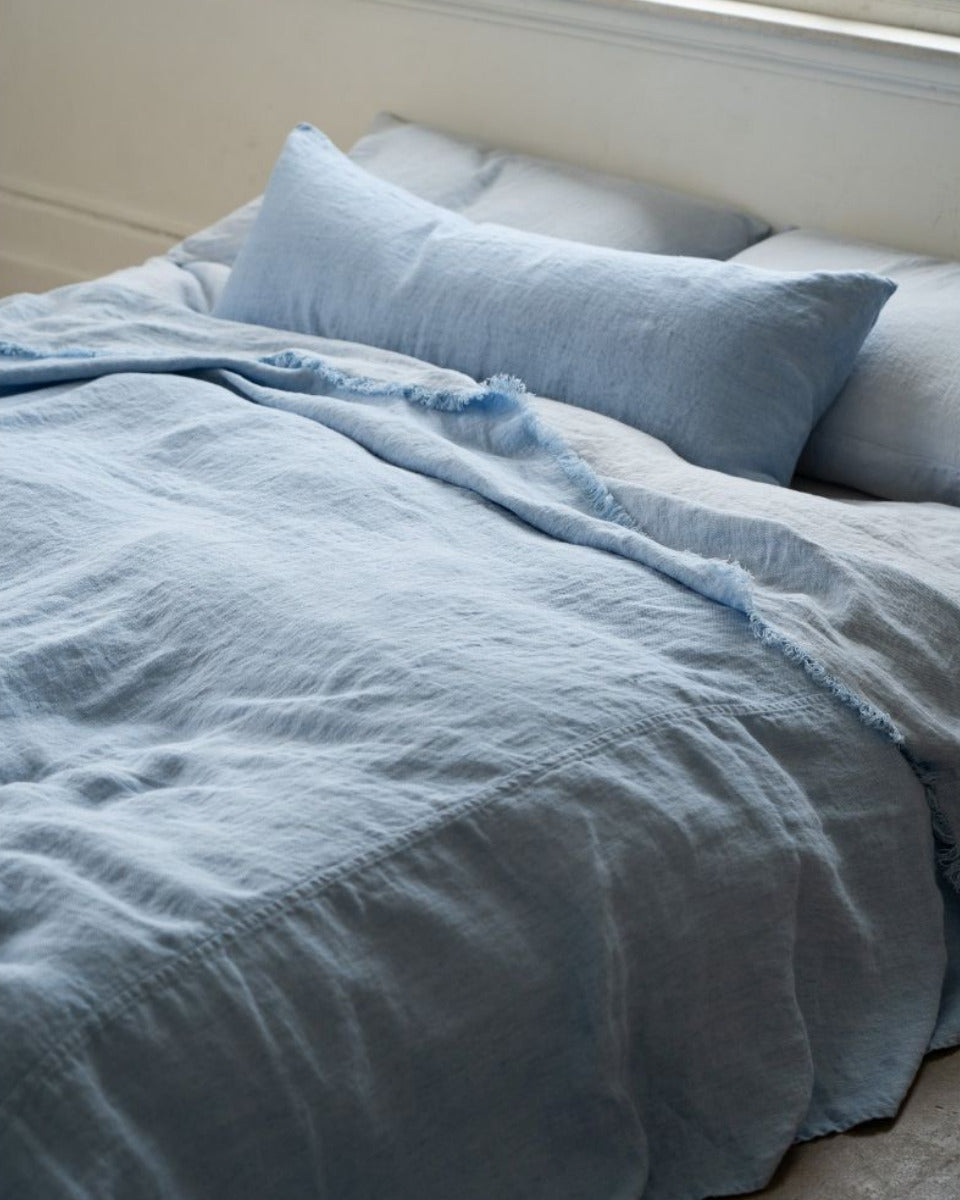 Blue bedding set on a bed in a room with a window.