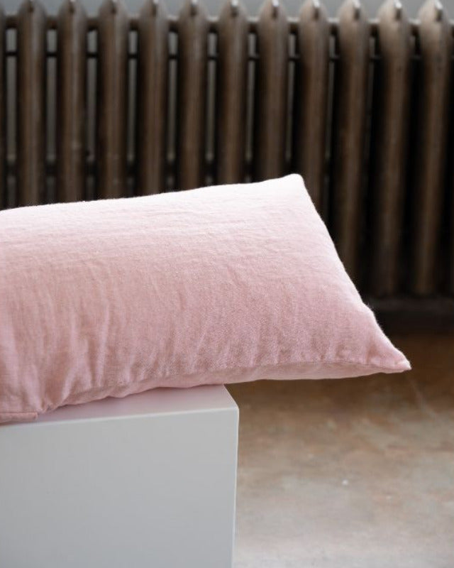 Pink pillow on a white surface with a radiator in the background