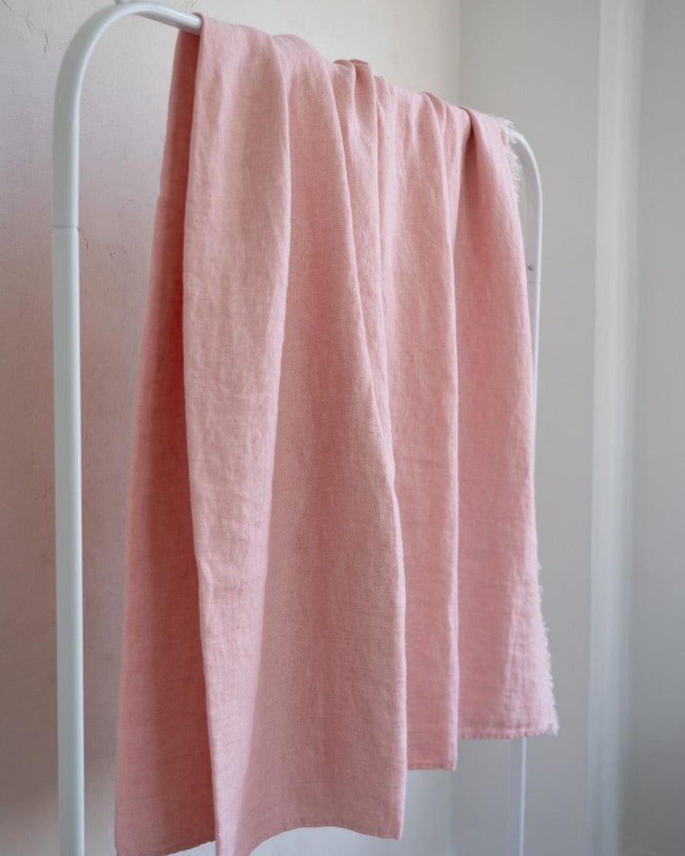 Pink towel hanging on a white rack against a light gray wall.
