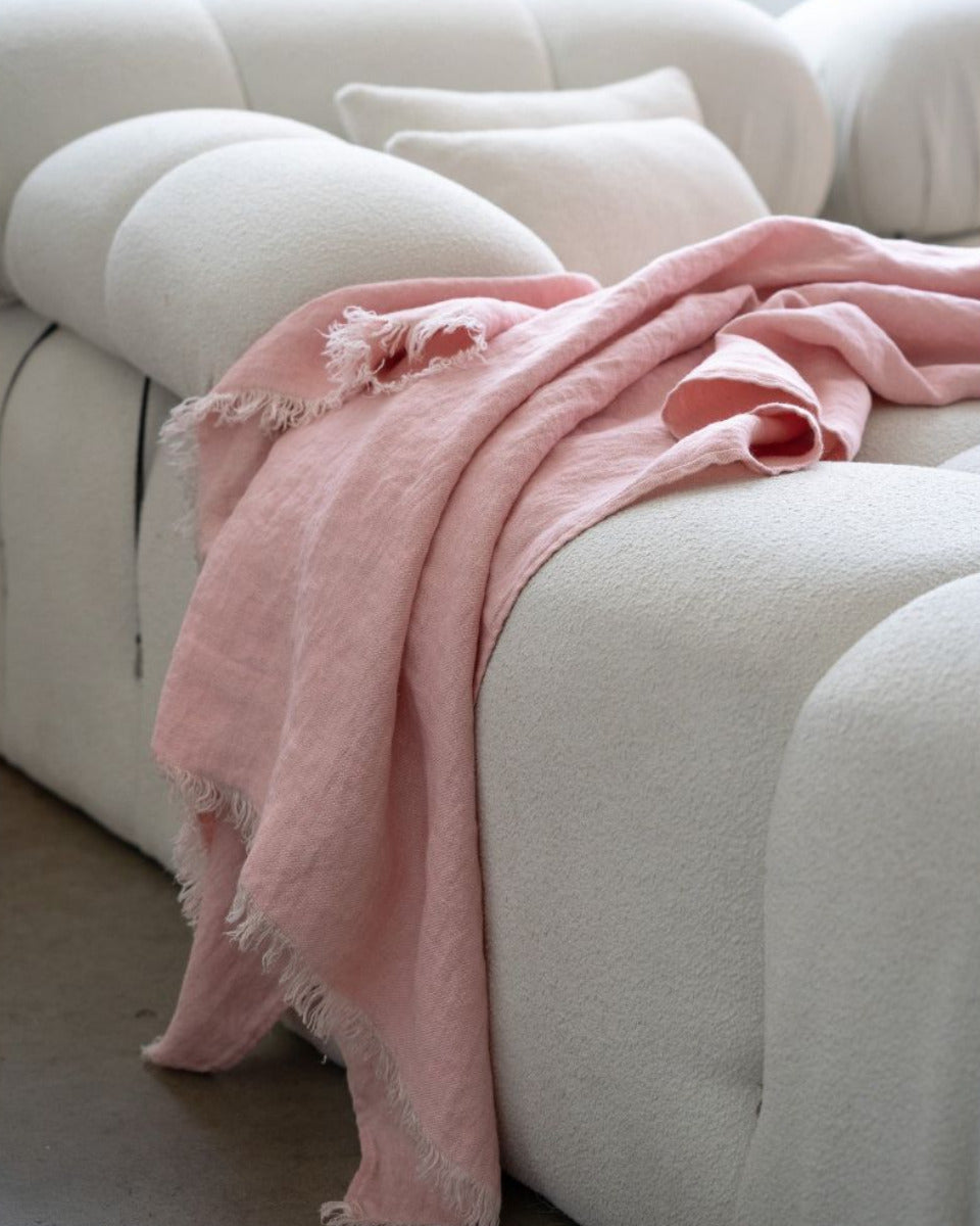 Pink blanket draped over a white sofa with a neutral background