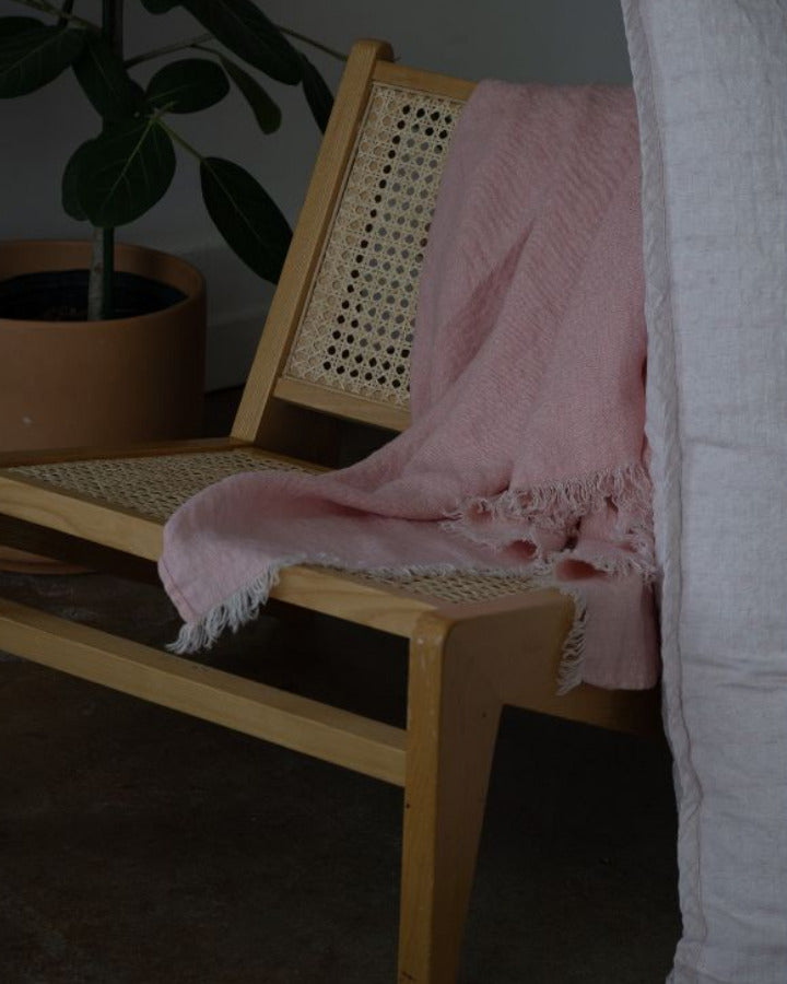 Wooden bench with a pink blanket draped over it in a dimly lit room.