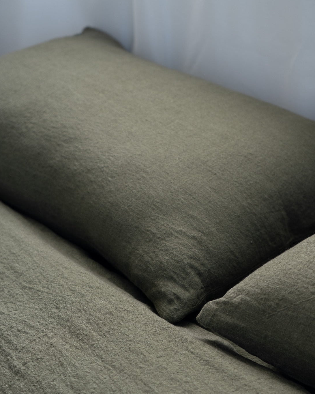 Two green pillows on a bed against a white wall