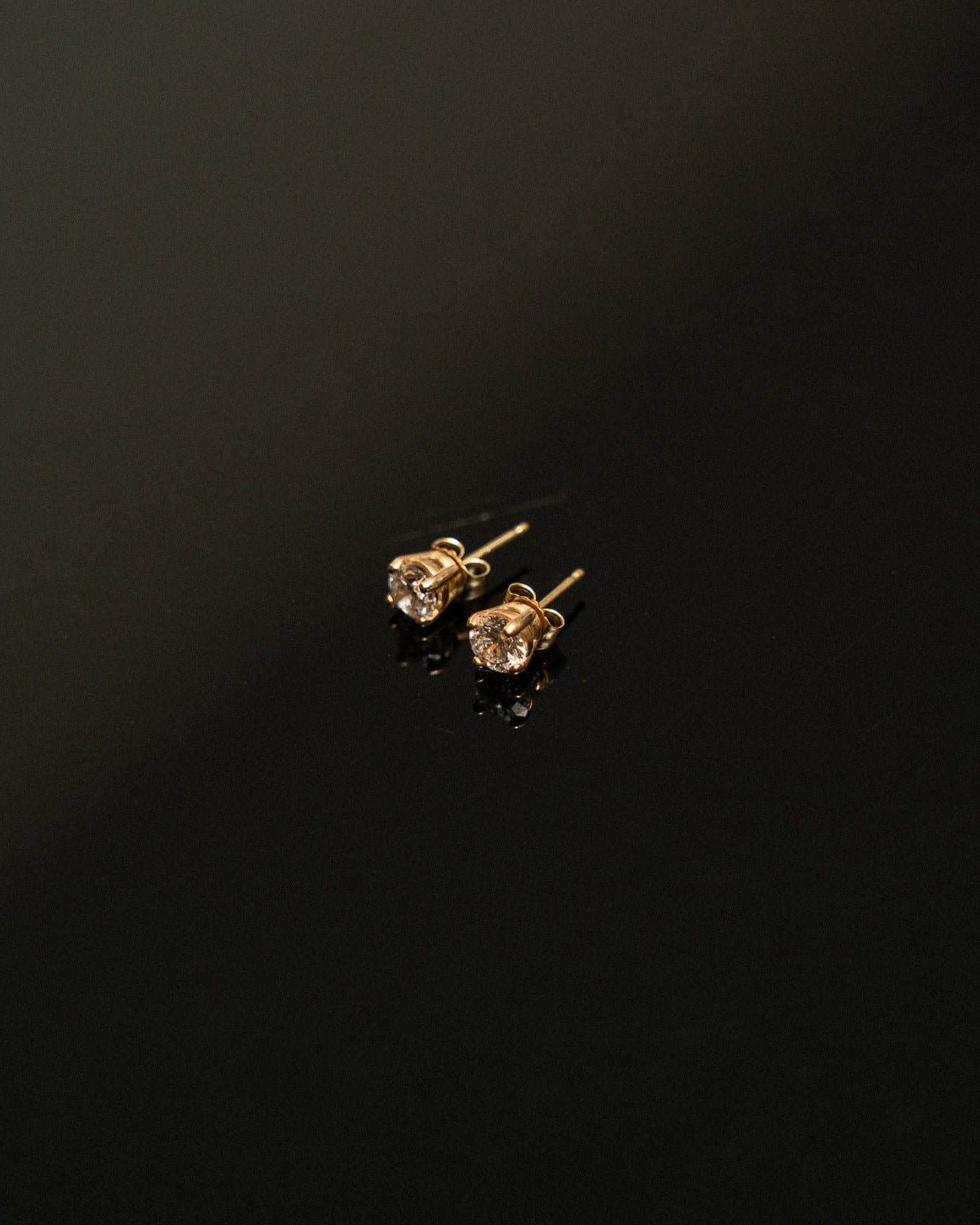 Pair of gold diamond stud earrings on a black background