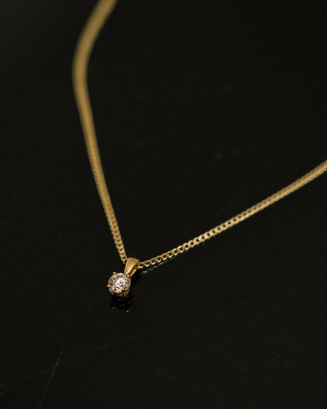 Gold necklace with a small diamond pendant on a black background