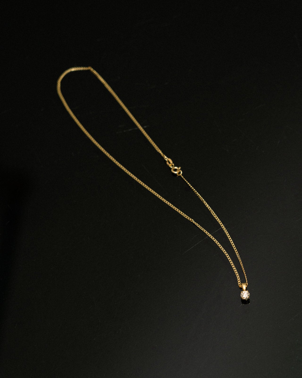 Gold necklace with a small pendant on a black background