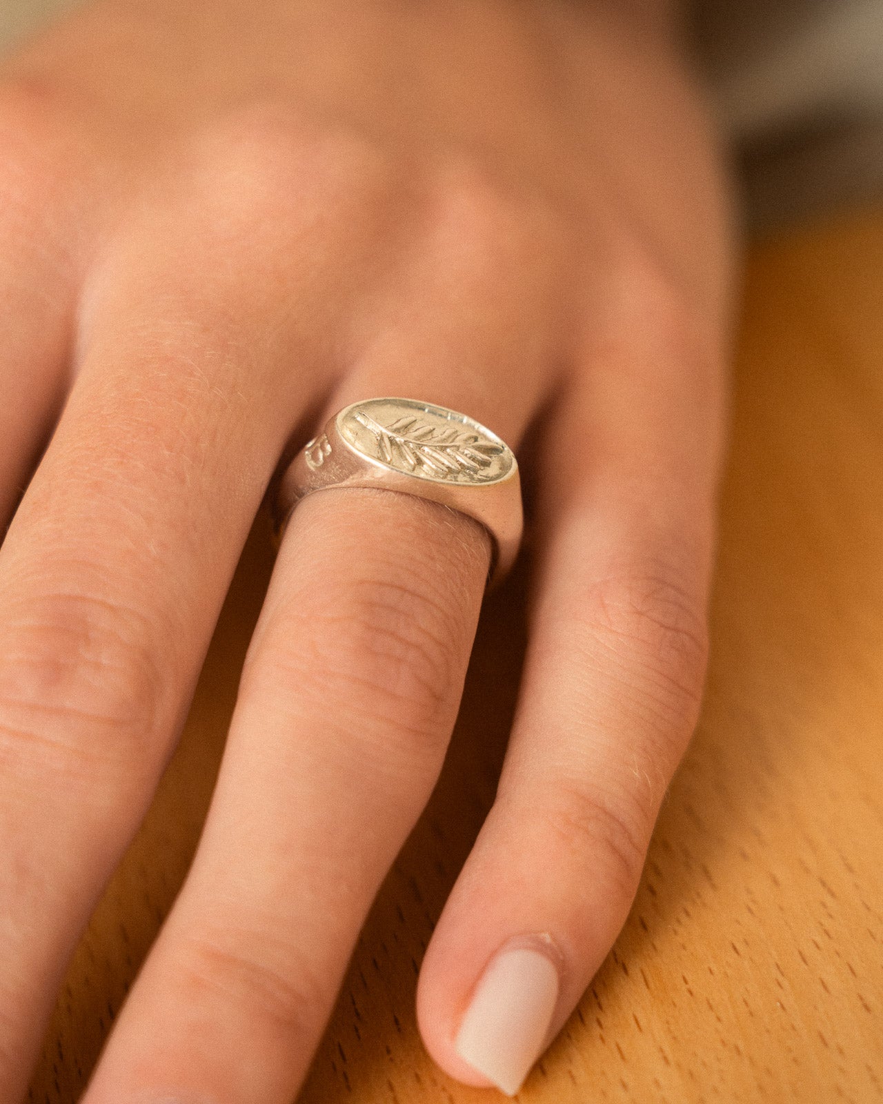 Sterling Silver ring with fern design on a person's finger against a wooden background
