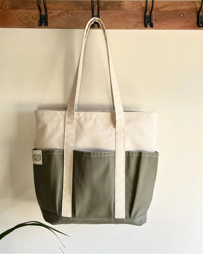 green and white Rather green amiga tote bag hanging on a wooden rack with hooks.